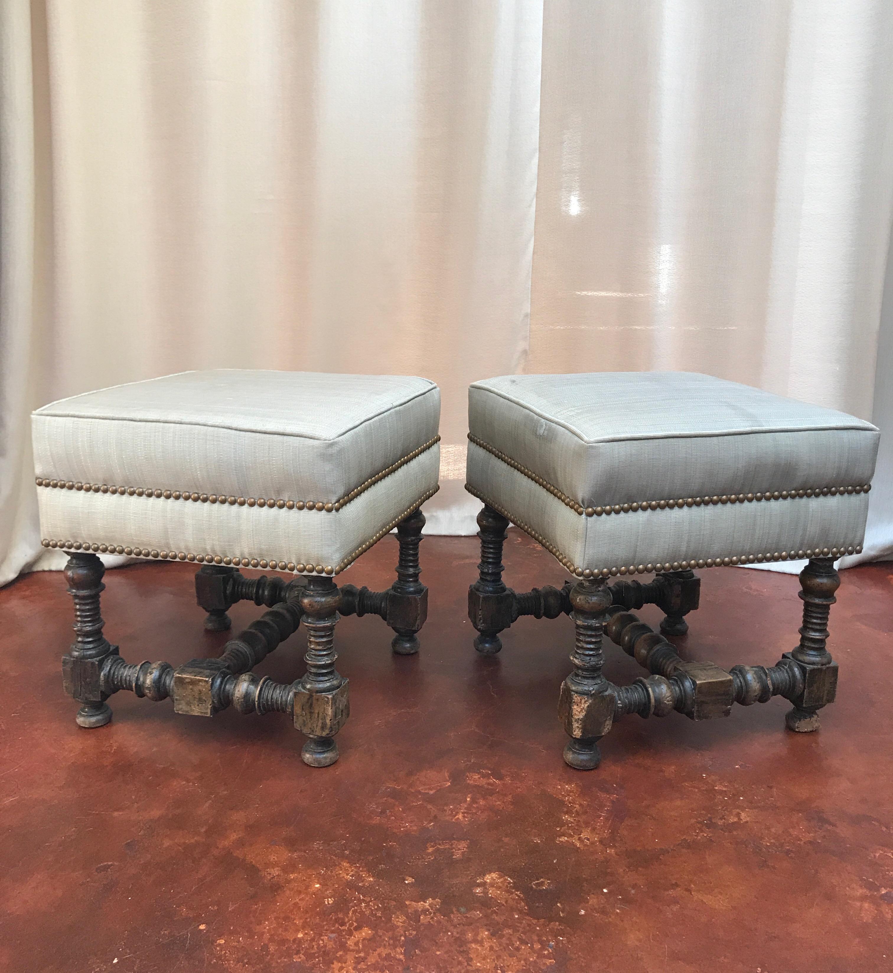 An early pair of Jacobean walnut stools from the 18th century. They are covered in a light blue horse hair fabric with nail head trim with some spots on the coverings.  There is some damage to the wood but they are still sturdy and have a great look.