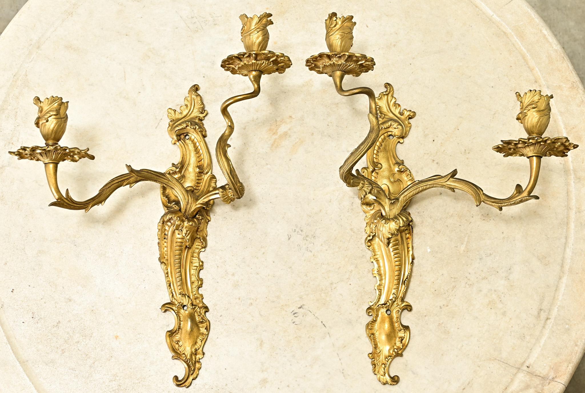 An elegant pair of French Louis XV period brass sconces. This stunning pair of non wired sconces are made of solid brass. The stylized backplate has all the classic Rococo patterns found in the Louis XV style. Twisting and vine-like arms end with