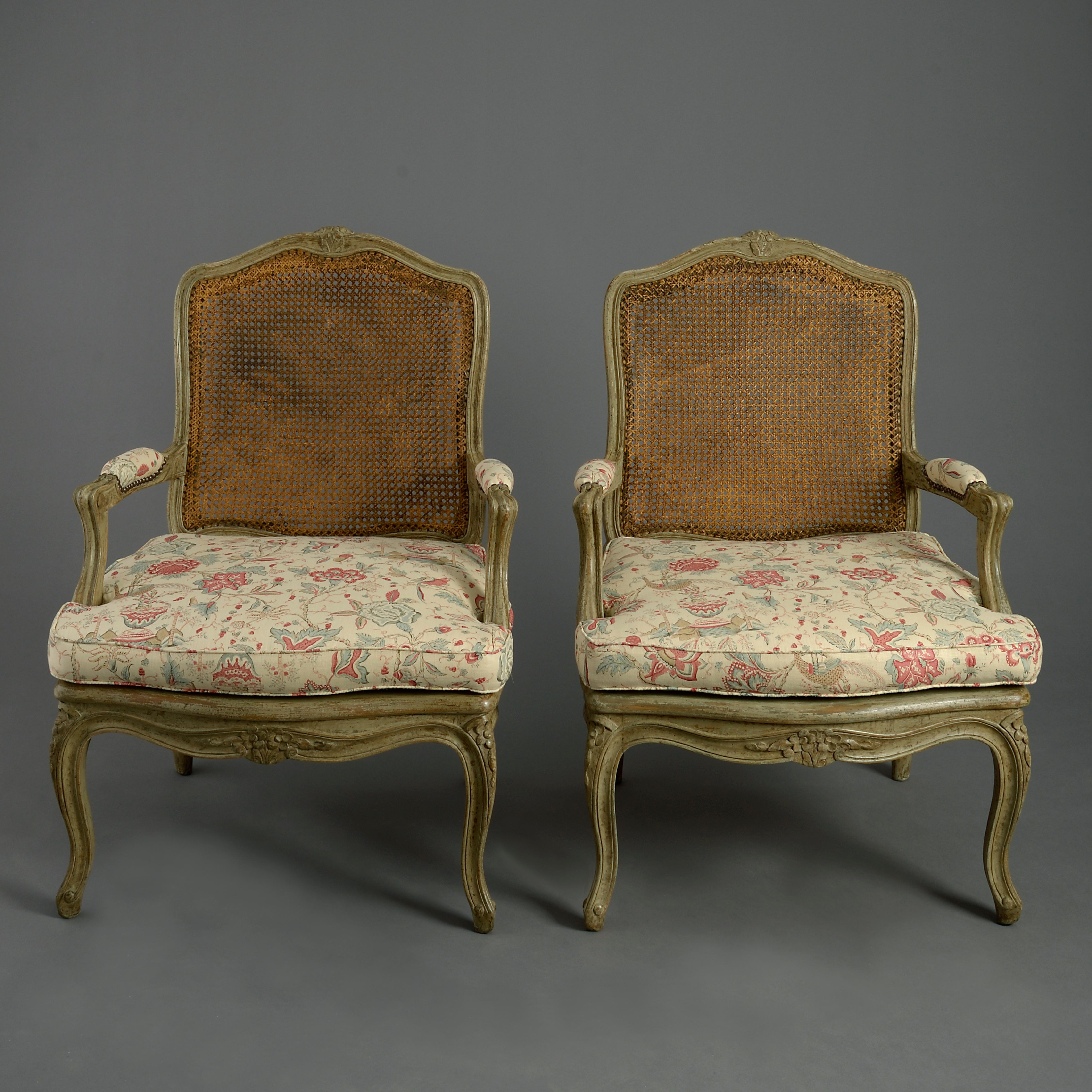 A fine pair of mid-18th century Louis XV period painted fauteuils or open armchairs in the Rococo taste, the cartouche backs and seats with cane work, the arms with upholstered rests, the cresting’s, front seat rails and cabriole legs carved with