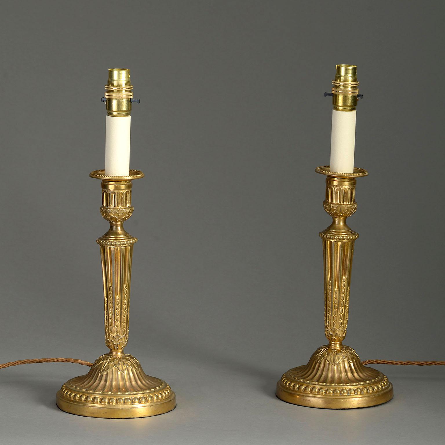 A pair of late 18th century ormolu candlesticks, the detachable socles set within urn shaped holders, raised on tapering stop-fluted stems, terminating on circular bases with beaded rims. Now mounted as lamp bases.

Dimensions refer to whole lamp
