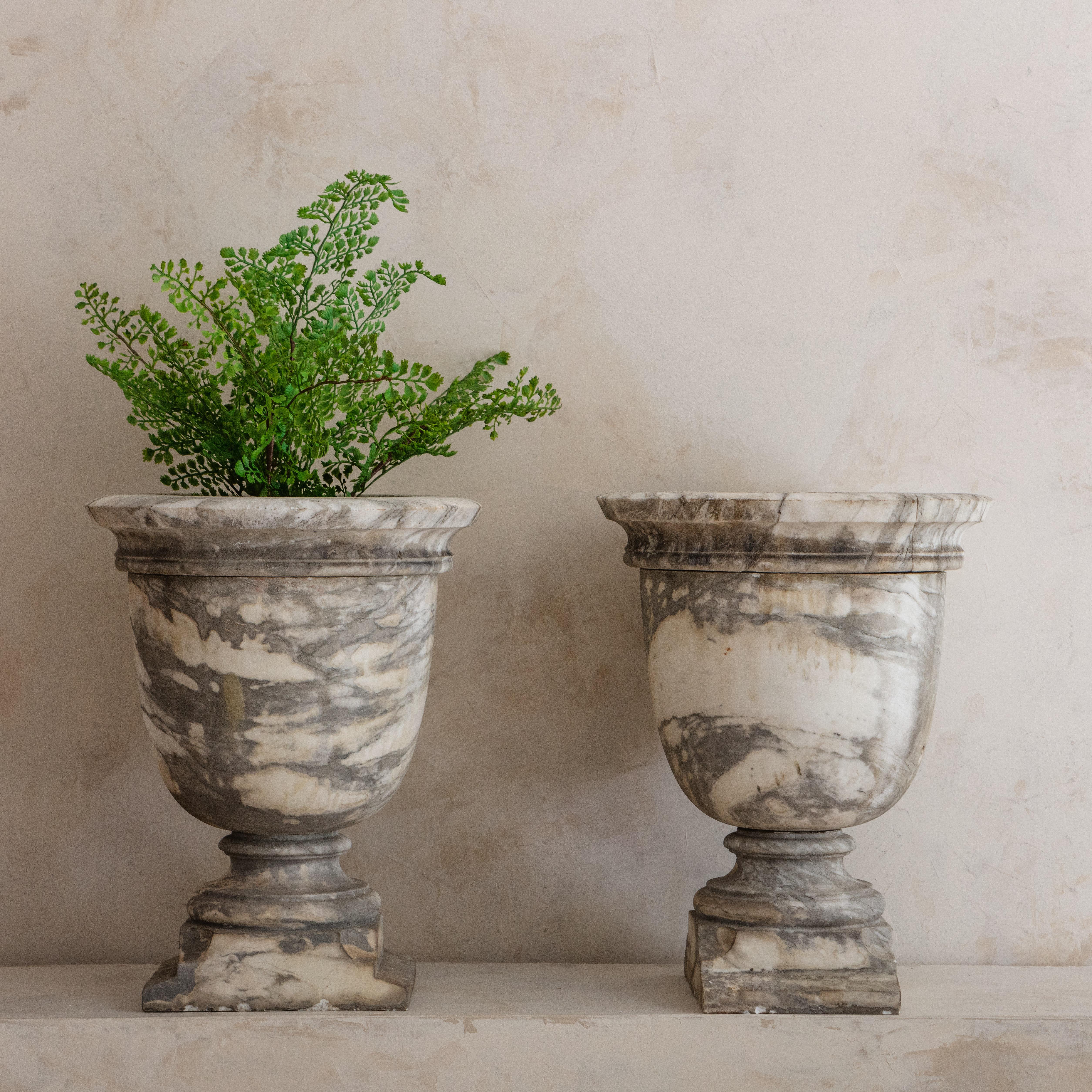 A unique pair of marble urns source in Paris, France. Feauturing a stunning honed white marble with heavy deep gray veining. Each urn has an interior diameter of 6.75” and 6.75” deep.