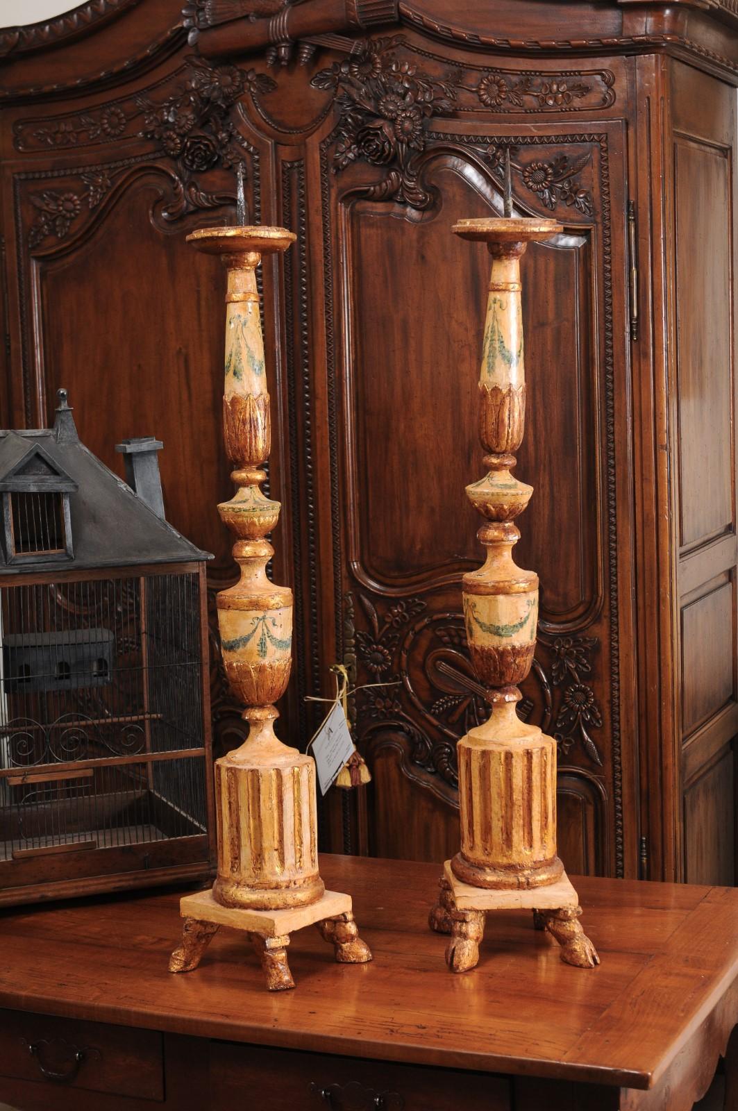 A pair of Italian neoclassical period painted and gilded candlesticks from the 18th century, with fluted motifs and hoof feet. Created in Italy during the later years of the 18th century, each of this pair of candlesticks features a painted body