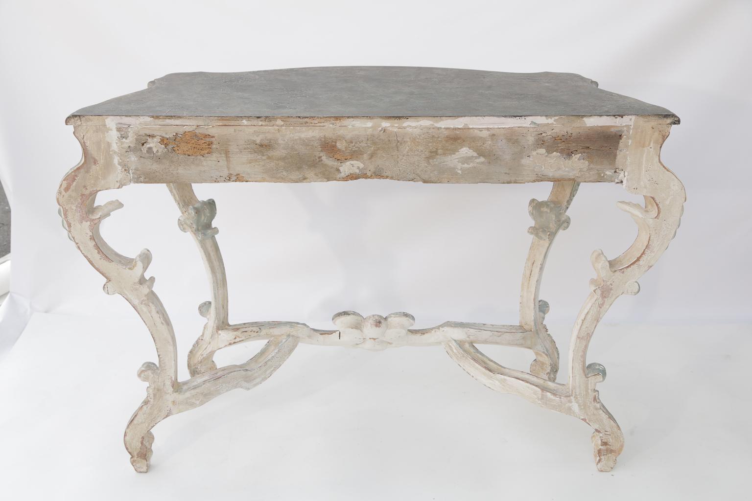 Pair of Rococo consoles, each having a shaped, faux-painted top, on a painted frame showing natural wear, the table base with pierced carvings in high Rococo relief, with very large, carved foliage rocaille and scroll work to its apron, the