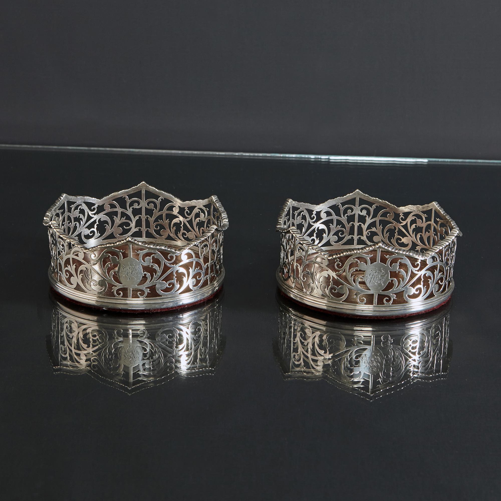Pair of lovely antique silver wine bottle or decanter coasters, with hand-pierced openwork sides, decorated with a scrolling leaf design and their original wood bases. The scalloped borders feature applied gadroon pattern mounts and each has a