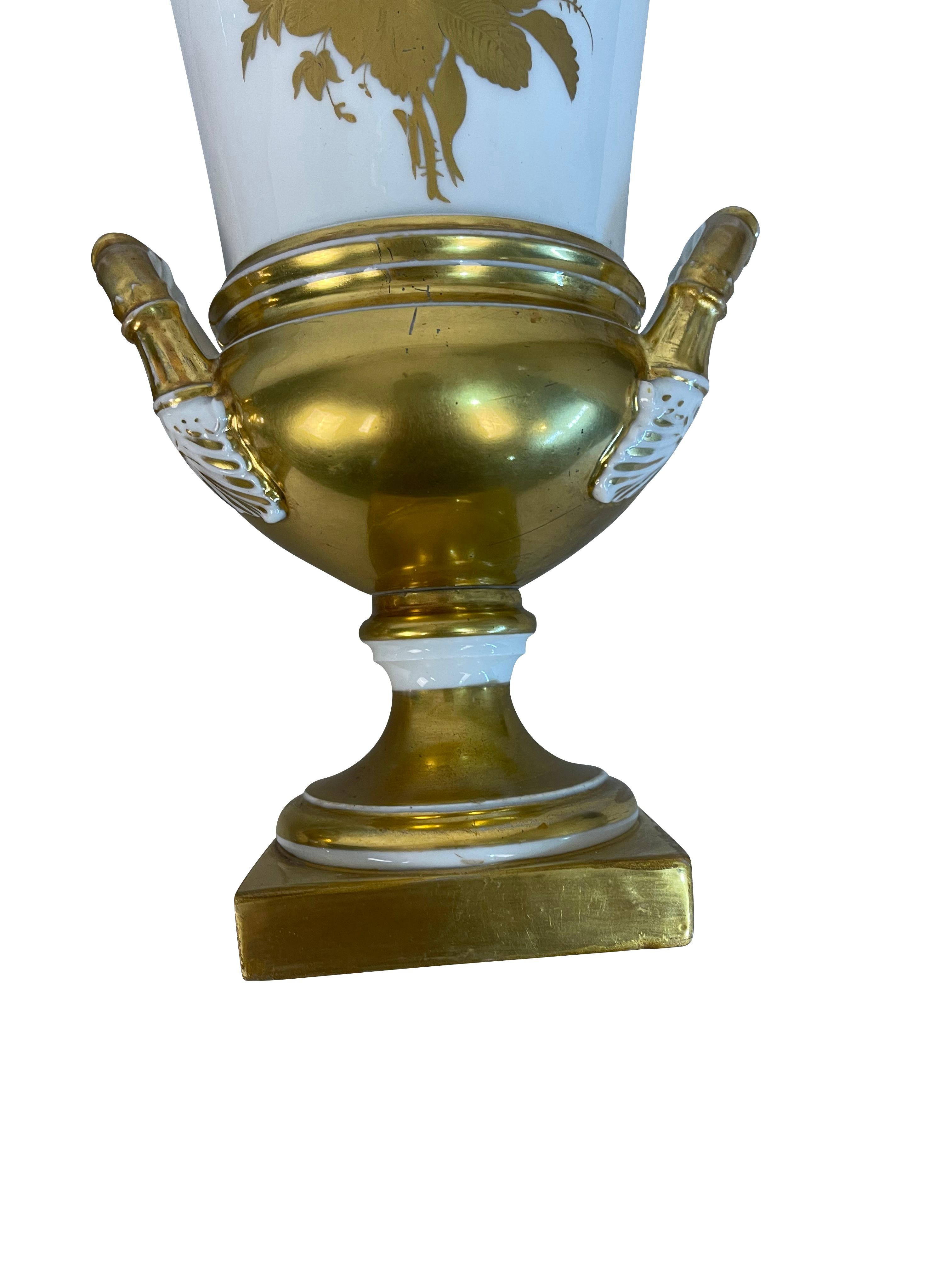 Pair of Porcelain de Paris French white and gold gilt urns with floral design. A lovely hand-painted gilt floral bouquet on the front and back. The vases sit on square gilt bases that rise to a classical urn form vase with gilded handles on both