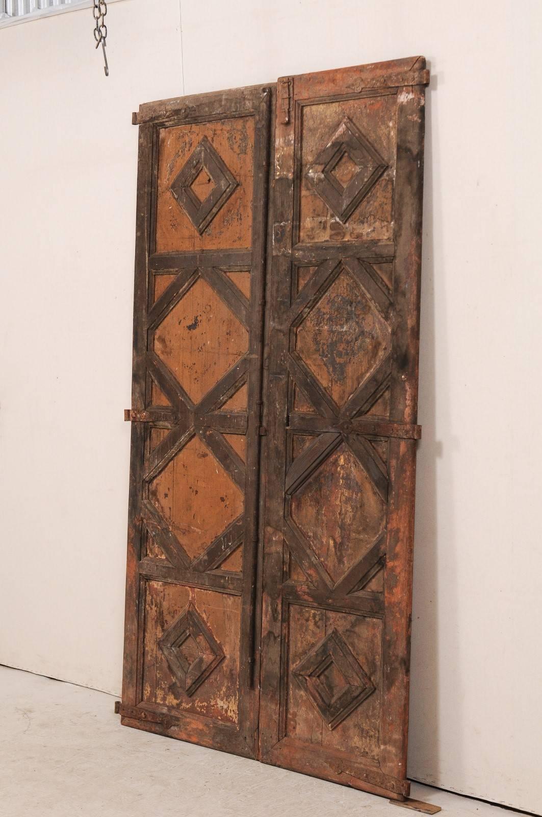 A pair of 18th century Spanish wood doors. This pair of antique Spanish doors feature recess panels on their front sides, thickly molded, creating a vertically lined diamond pattern. The doors retain their old iron hardware, paint and finish, which