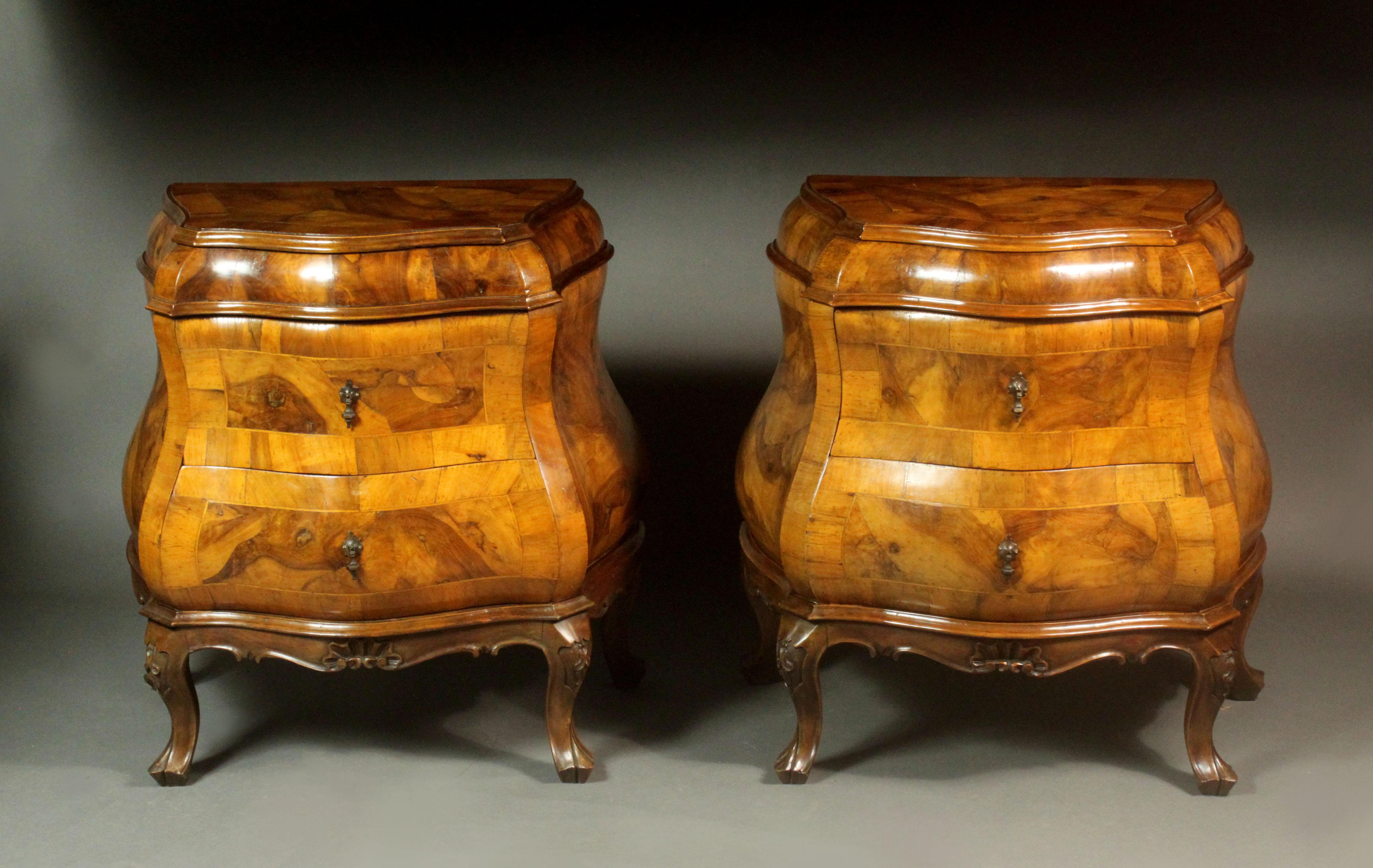An unusual pair of late 18th century style bombay front bedside chests in veneered walnut of a good colour.  Each has two drawers with the original drop handles and the top does not open upwards, it is fixed. Well carved small cabriole legs with a