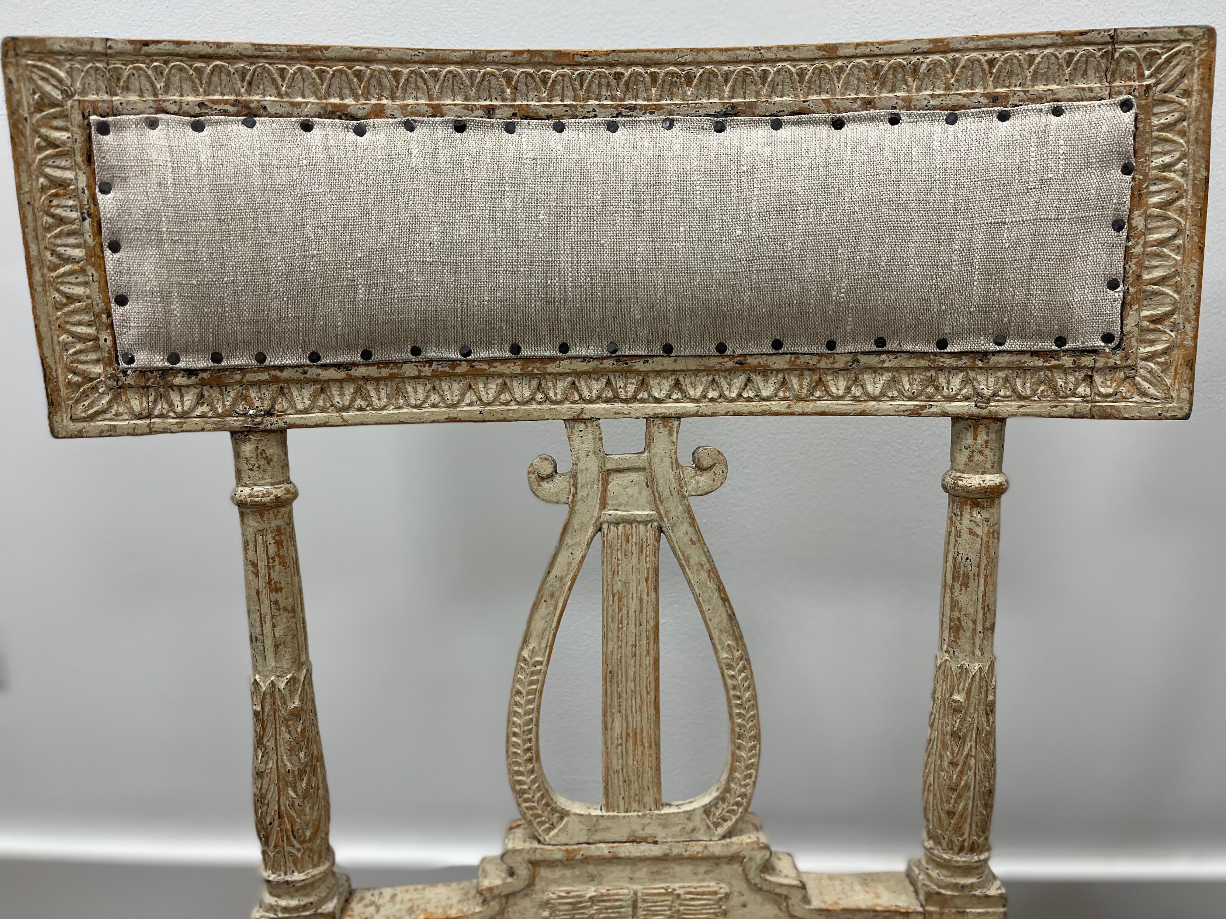 An unusual pair of intricately hand-carved provincial Swedish Gustavian Lyre chairs. Featuring decorative leaf cut raised backs atop tapered, fluted and elongated leaf cut sides and a demure harp-shaped center piece with leaf cut and reeded