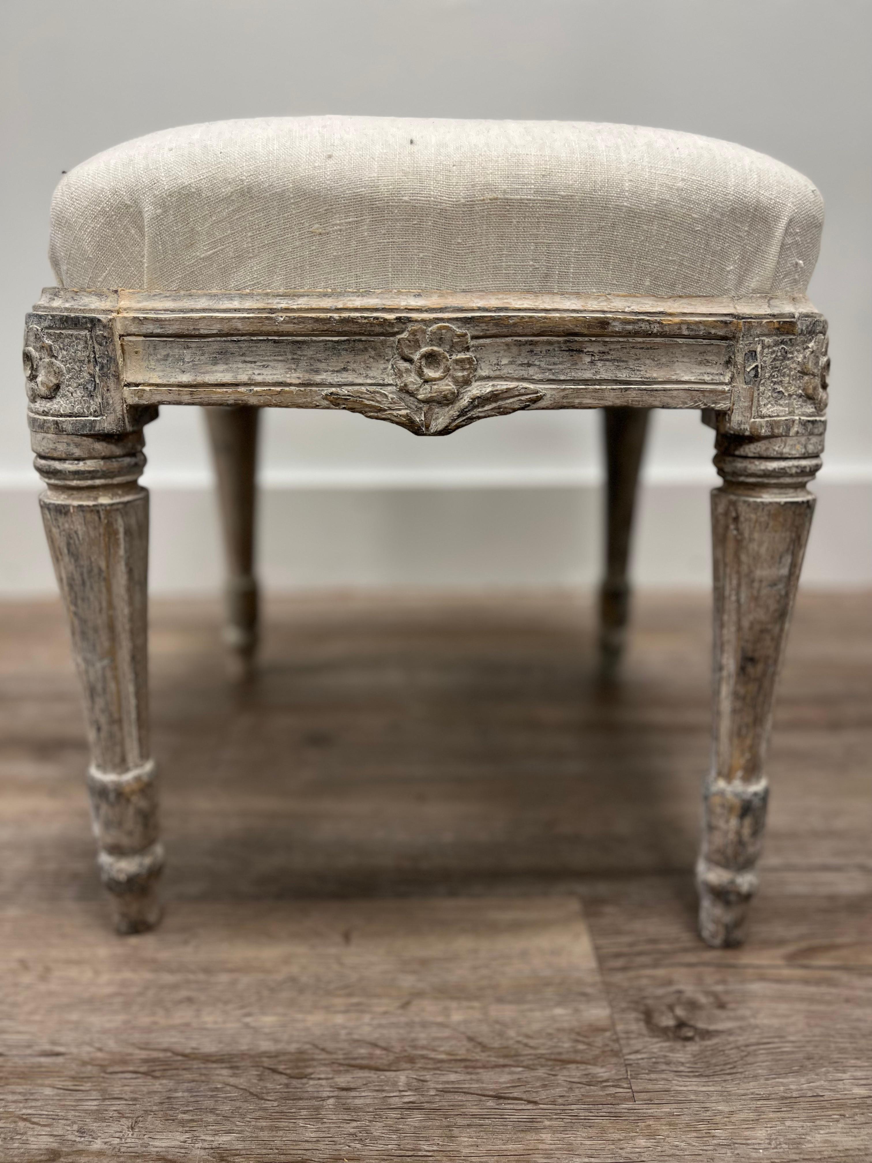 An unusual pair of Rococo-Gustavian transitional footstools made in Stockholm. The base has rounded fleurons on the corners and a flower-leaf carving in the bowed center. The legs are turned, tapered and fluted. This piece has older grey paint and