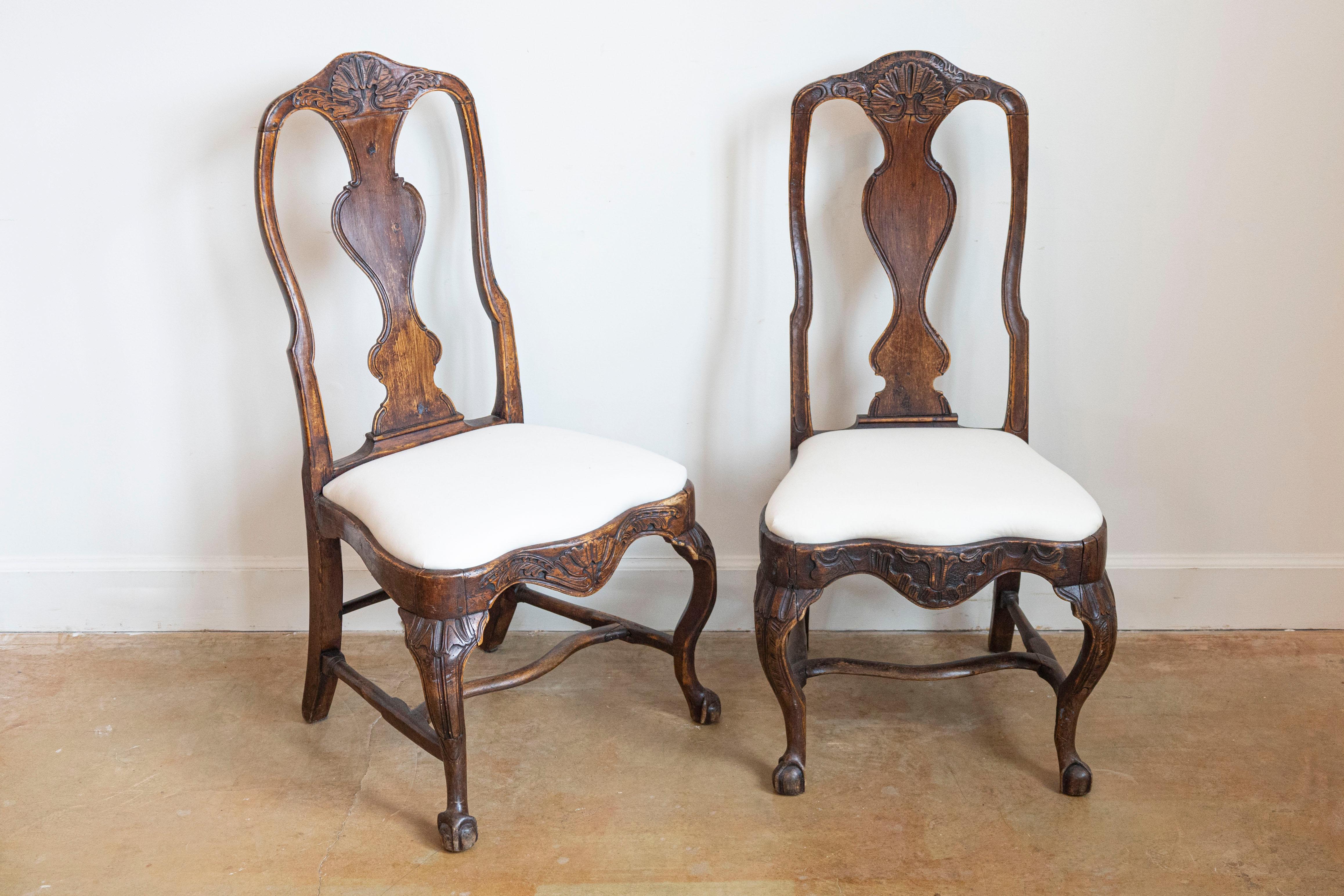 A pair of Swedish Rococo period walnut side chairs from the 18th century, with upholstery and cabriole legs. Created in Sweden during the 18th century, each of this pair of Rococo chairs features a curving pierced back with carved splat, sitting