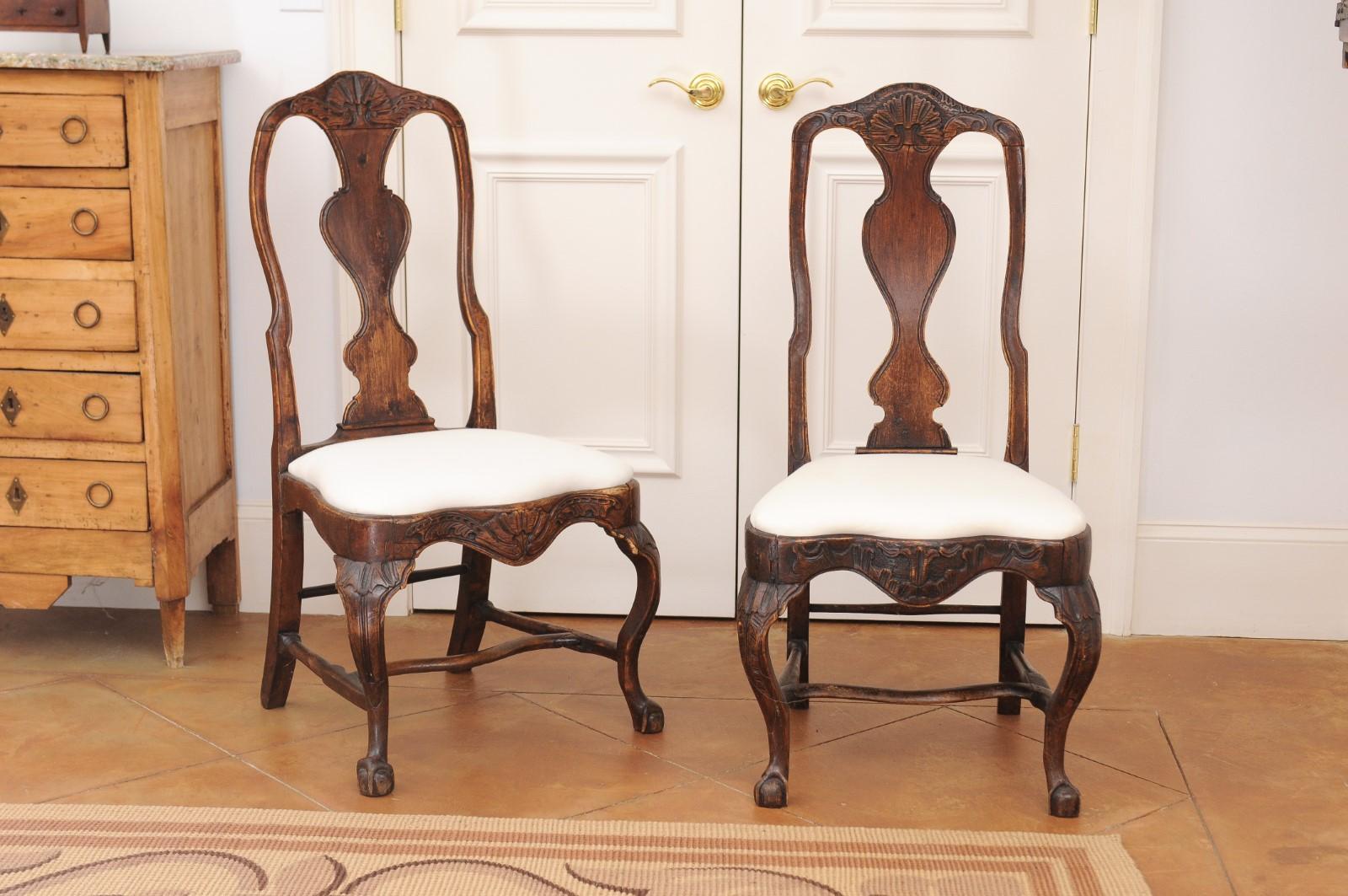 A pair of Swedish Rococo period walnut side chairs from the 18th century, with upholstery and cabriole legs. Created in Sweden during the 18th century, each of this pair of Rococo chairs features a curving pierced back with carved splat, sitting
