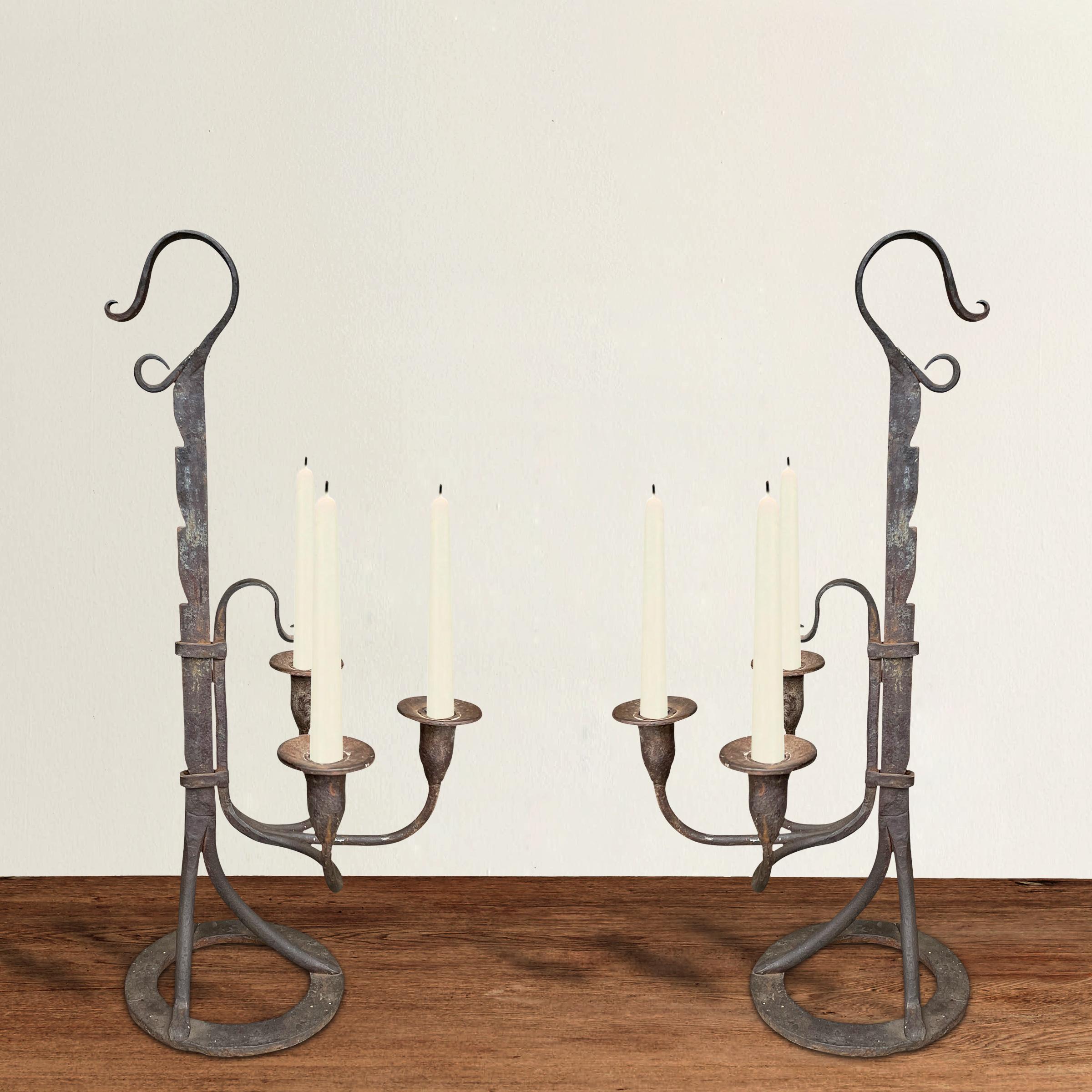 An incredible pair of 18th century American wrought iron three-arm candelabra each adjustable in height by pulling the arms up the ratchet stems, and resting on round disc feet. Charming and strong in design!
