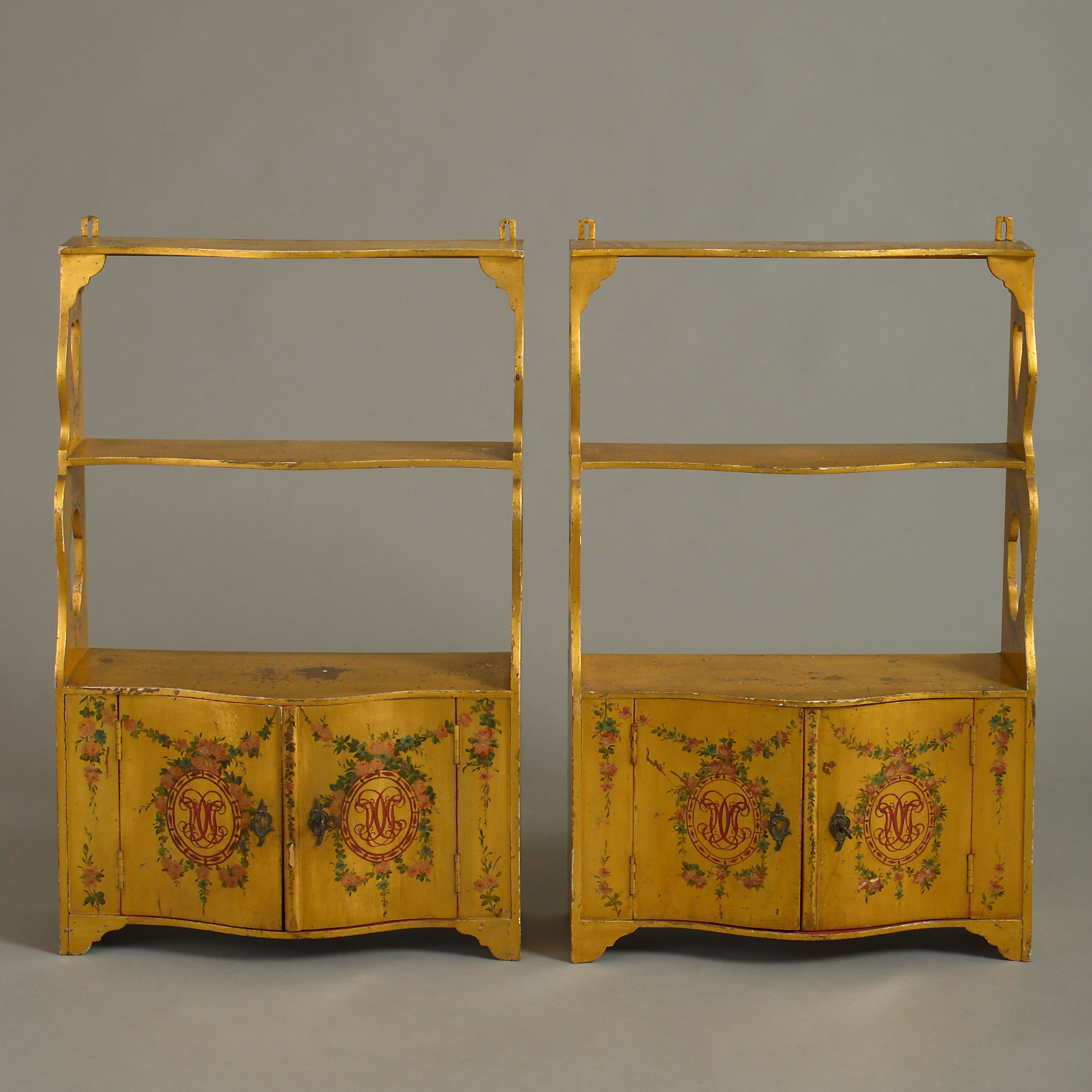 A pair of 18th century ochre yellow painted waterfall hanging shelves, having pierced sides and each with serpentine cupboard doors opening to reveal red painted interiors with additional shelves, the exteriors with foliate polychrome decoration and