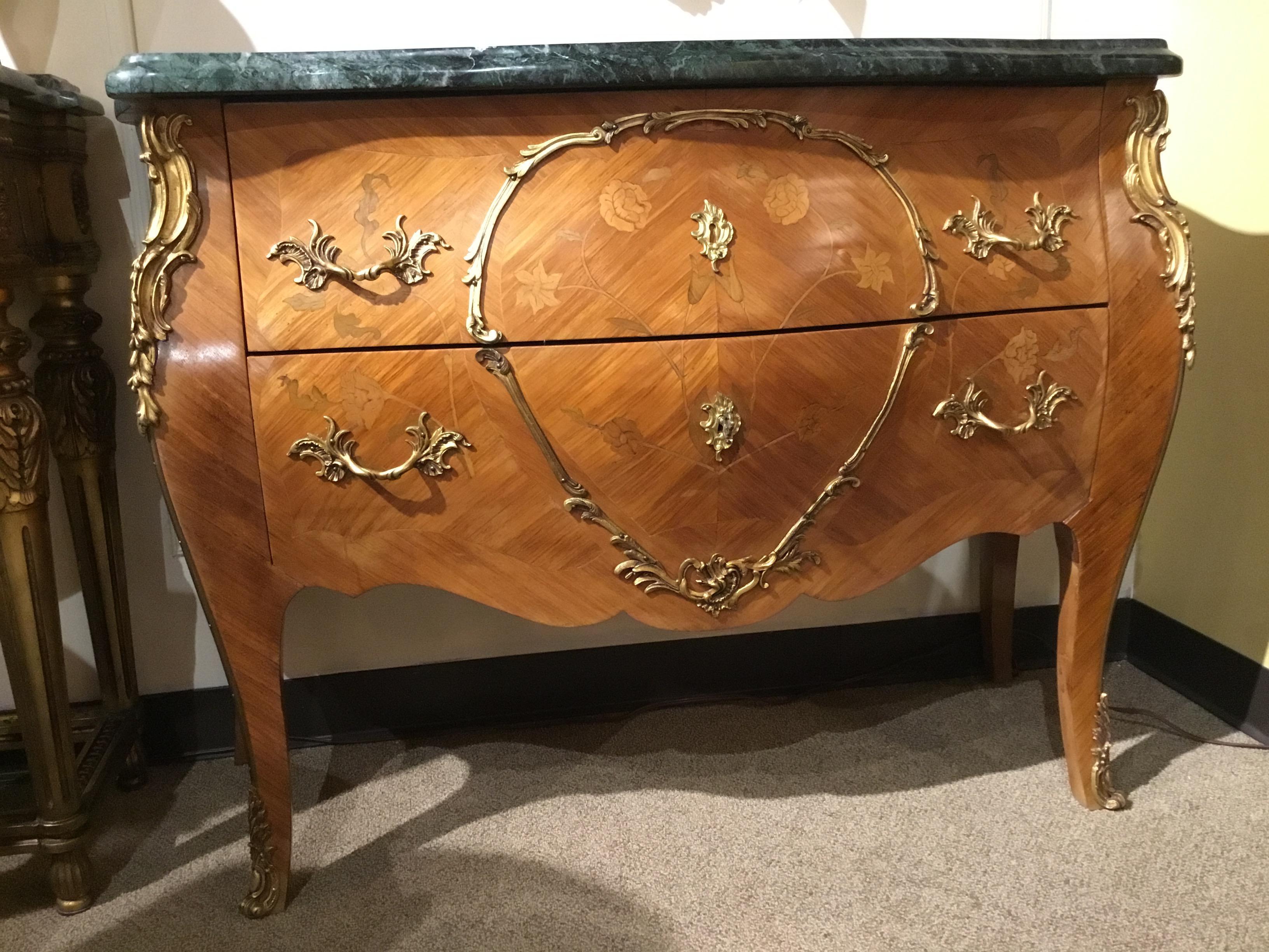 Serpentine fronted marble top and bombe form, fitted with two drawers mounted with gilt bronze
Trim, pulls and escutcheons. Accented with floral inspired marquetry inlays. The contoured
Corners with foliate bronze appointments ending in cast