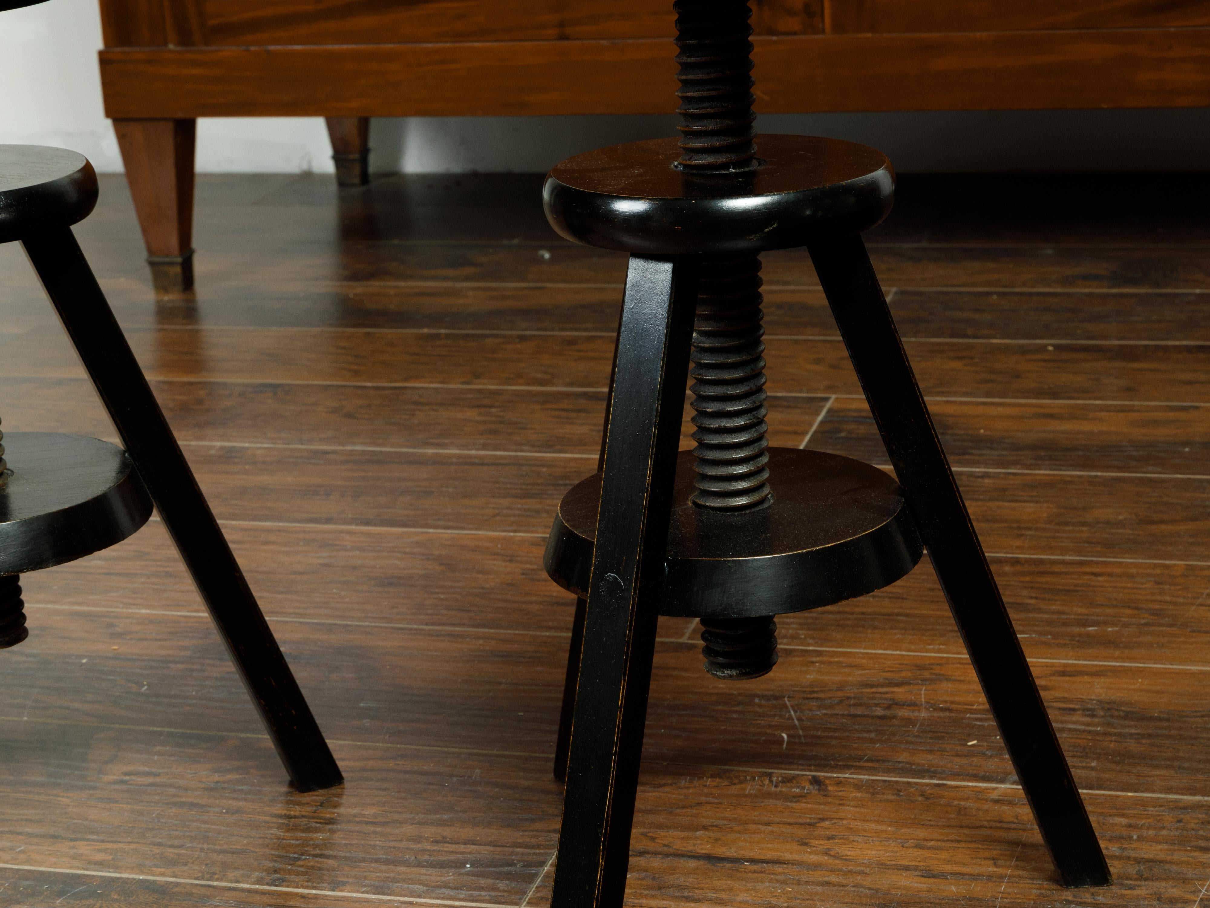 A pair of American adjustable artist's stools from the early 20th century, with black finish. Made in the USA during the first quarter of the 20th century, each of this pair of stools features a circular top resting on an adjustable base raised on
