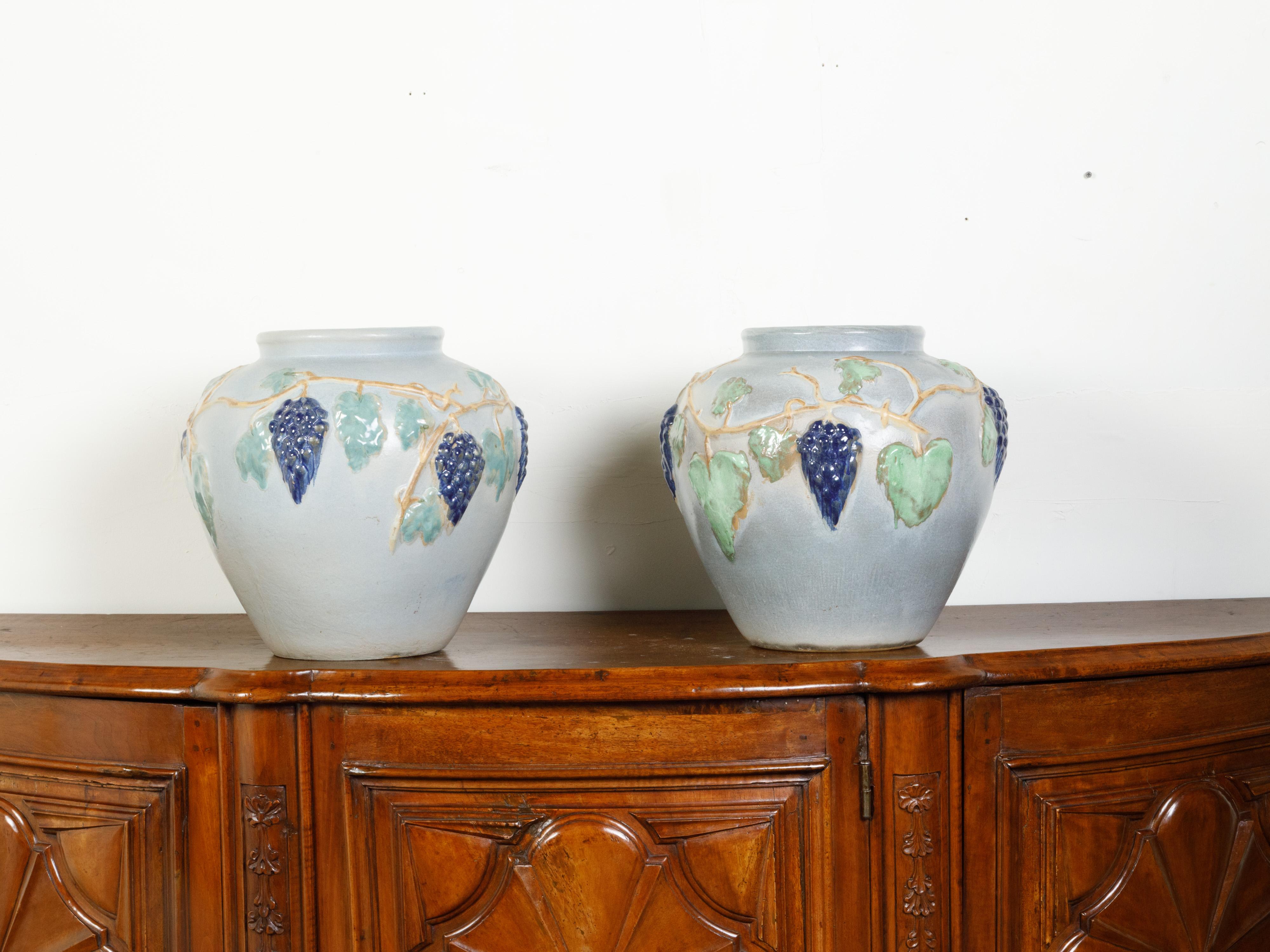 Ein Paar amerikanischer Steingut-Töpferwaren aus dem frühen 20. Jahrhundert mit Traubenmotiven. Jedes dieser Töpferwarenpflanzgefäße, die im ersten Viertel des 20. Jahrhunderts in den USA hergestellt wurden, fesselt unsere Aufmerksamkeit mit seinem