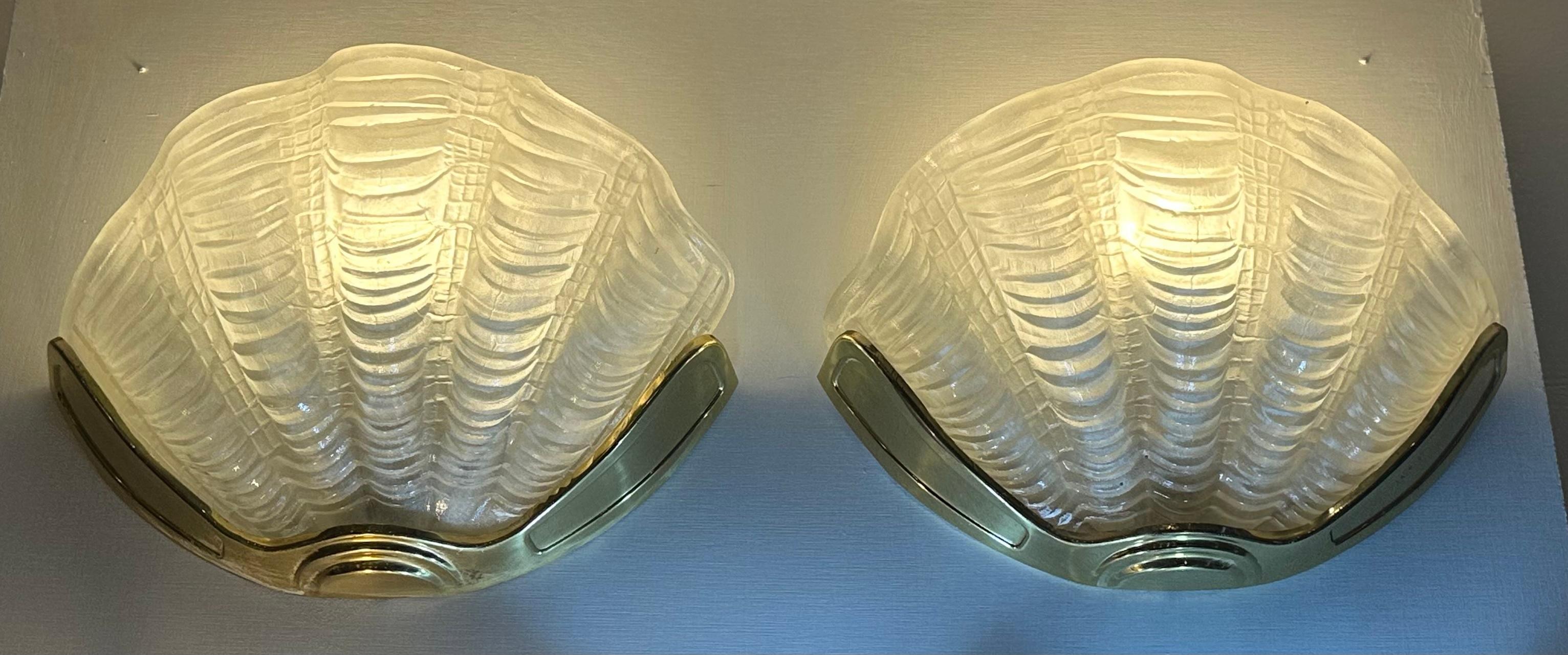 A pair of original 1920s Art Deco cinema clam shell wall lights. The white frosted rippled glass shades are mounted within a metal polished brass frame.  The shades cast a soft diffused light upwards illuminating the wall above beautifully.

The