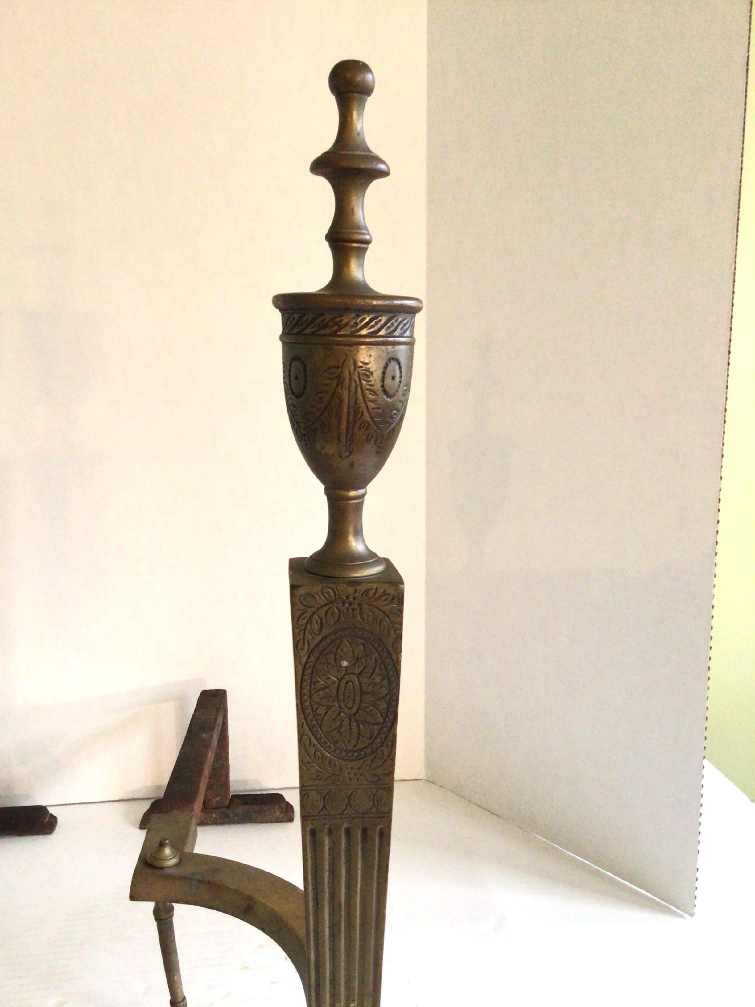 Personalize a fireplace with this elegant pair of 1920s Brass Andirons Elegantly engraved motifs are accented with Urns that sit atop stately fluted tapered columns
