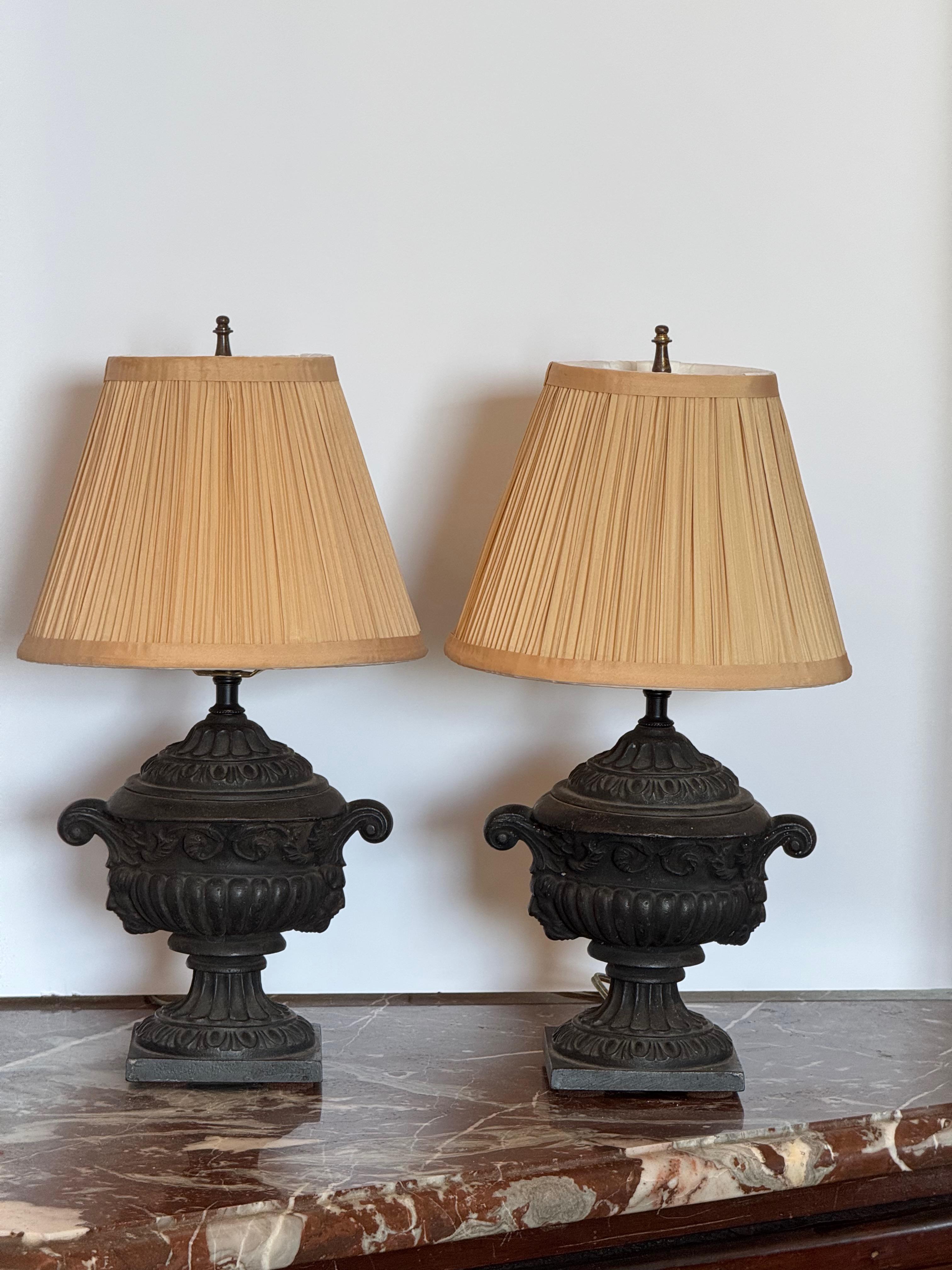 Heavy cast iron lamps in the form of classical urns with scrolled handles and acanthus details throughout. Set on square plinth bases and paired with pleated fabric shades. A bold, neoclassical presence for side tables or consoles.