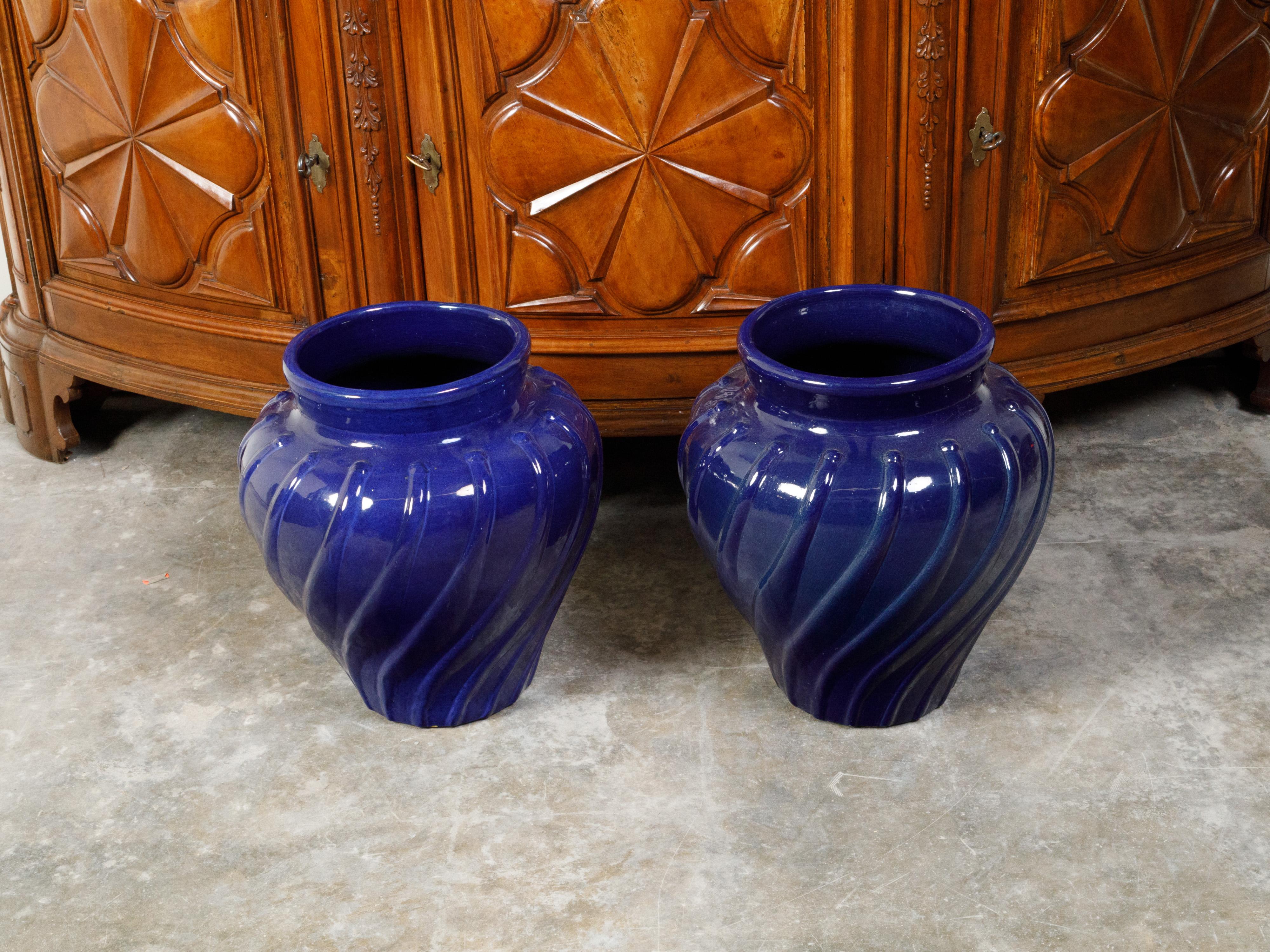 A pair of cobalt blue planters from the early 20th century, with wavy patterns. Created during the first quarter of the 20th century, each of this pair of planters features a generous tapering body adorned with a cobalt blue ground accented with