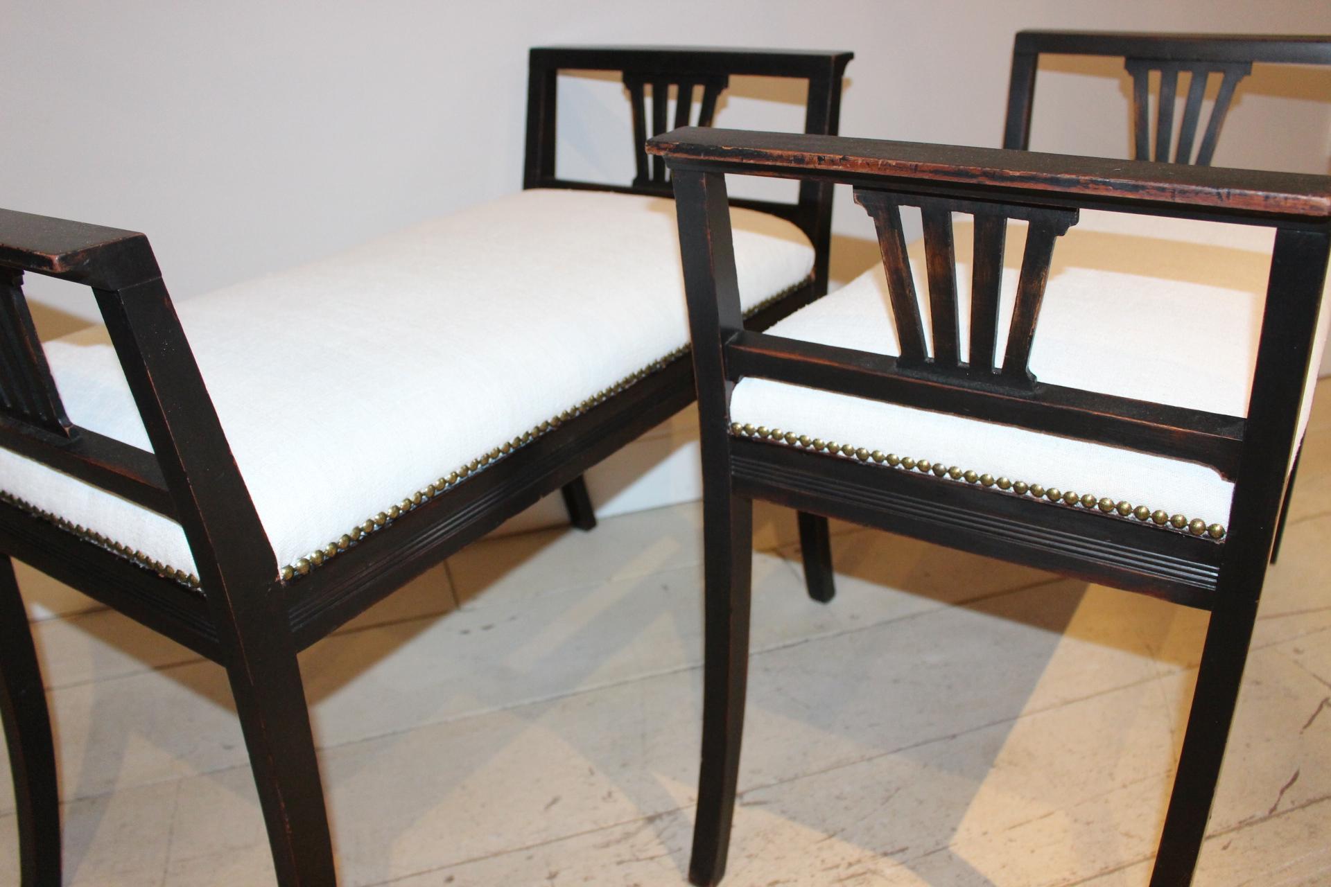 A striking pair of 1920s ebonized high-sided Swedish stools with arms. The stools are unusual due to their longer size and have been upholstered in a vintage French linen with gold speckled beading to the sides. The stools would work well in a