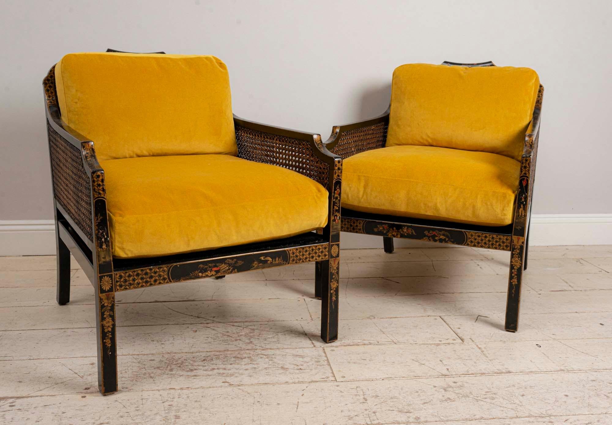 Pair of English 1920s Japanned armchairs with chinoiserie decoration, caned sides and back.
This chic pair of armchairs have wonderful saffron velvet upholstery with an additional small cushion for support. The armchairs would work well in both a
