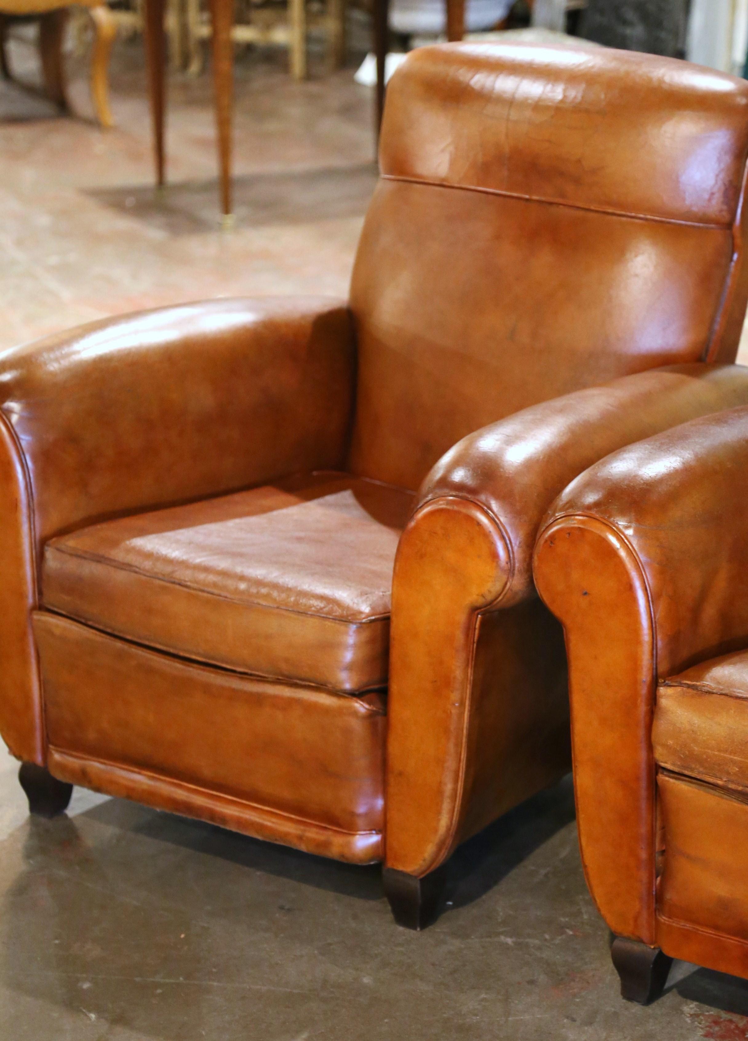 These Classic, antique Art Deco club chairs were crafted in France, circa 1920. The stately chairs feature wide, rounded armrests, a pitch back with an arched top shape, and square wooden feet at the base. The Classic, masculine French chairs are