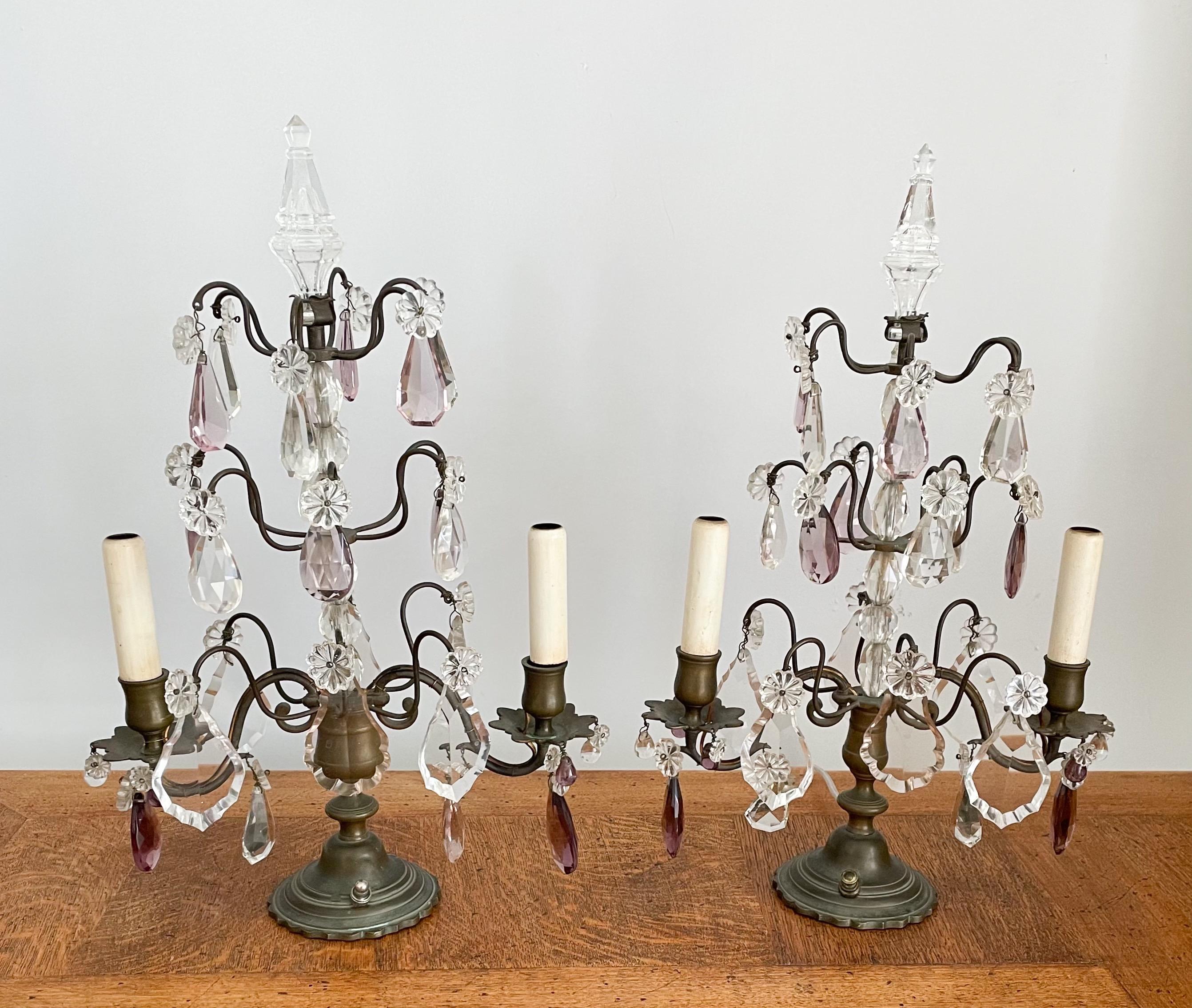 Gorgeous, 1920s French Louis XVI-style pair of bronze and crystal girandoles.

Each girandole consists of a delicate bronze frame embellished with faceted prisms in clear and light-amethyst tones. There is a hollow glass spike decorating the top