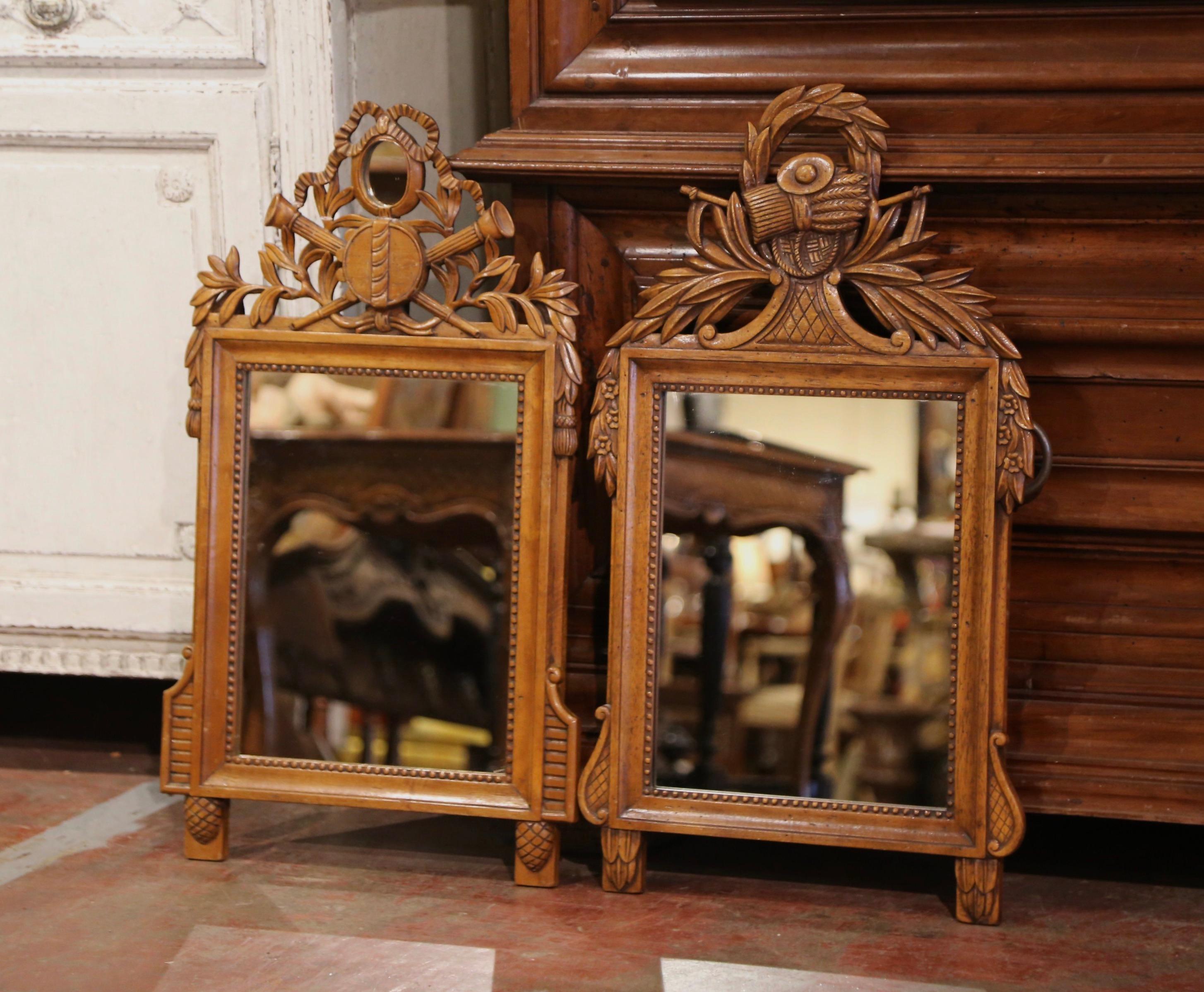 Decorate an entryway or hallway with this elegant pair of antique wall mirrors. Crafted of walnut wood in Southern France circa 1920, each mirror features hand-carved motifs at he pediment, including music instruments and the traditional Louis XVI