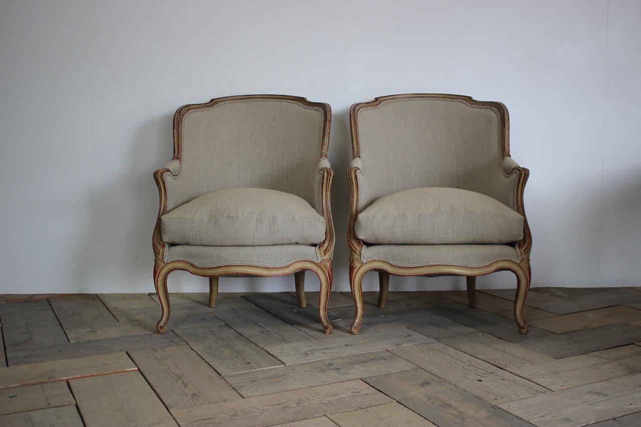 A very elegant pair of 1920s French painted armchairs in the Louis XVI taste, retaining the original decoration, having been reupholstered by us in a neutral linen with feather cushions.