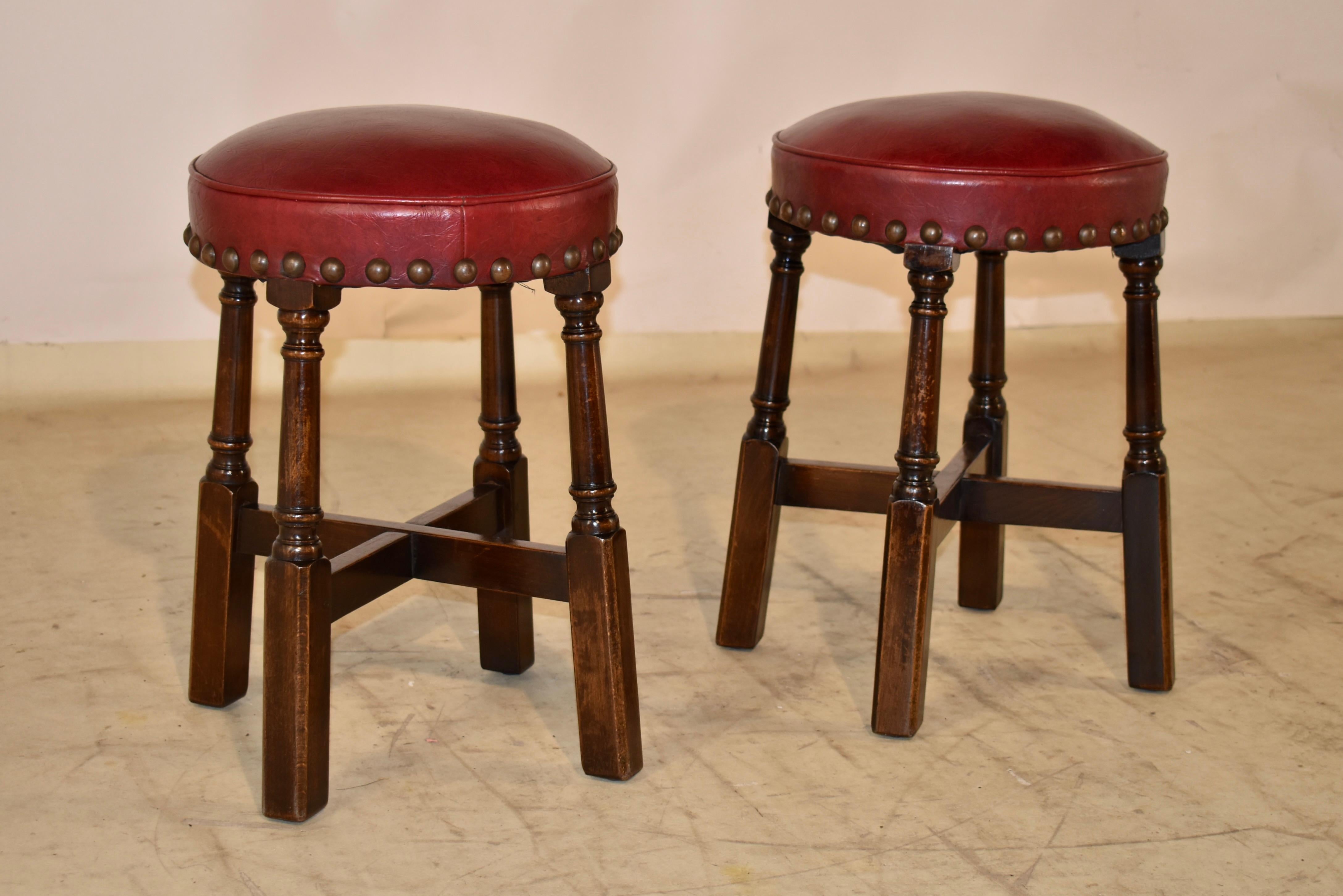 Pair of charming 1920's pub stools from England.  The seats are upholstered in what appears to be faux leather in a rich red color and finished around the base of the seat with brass tacks.  The base of the stool has nicely turned and slightly