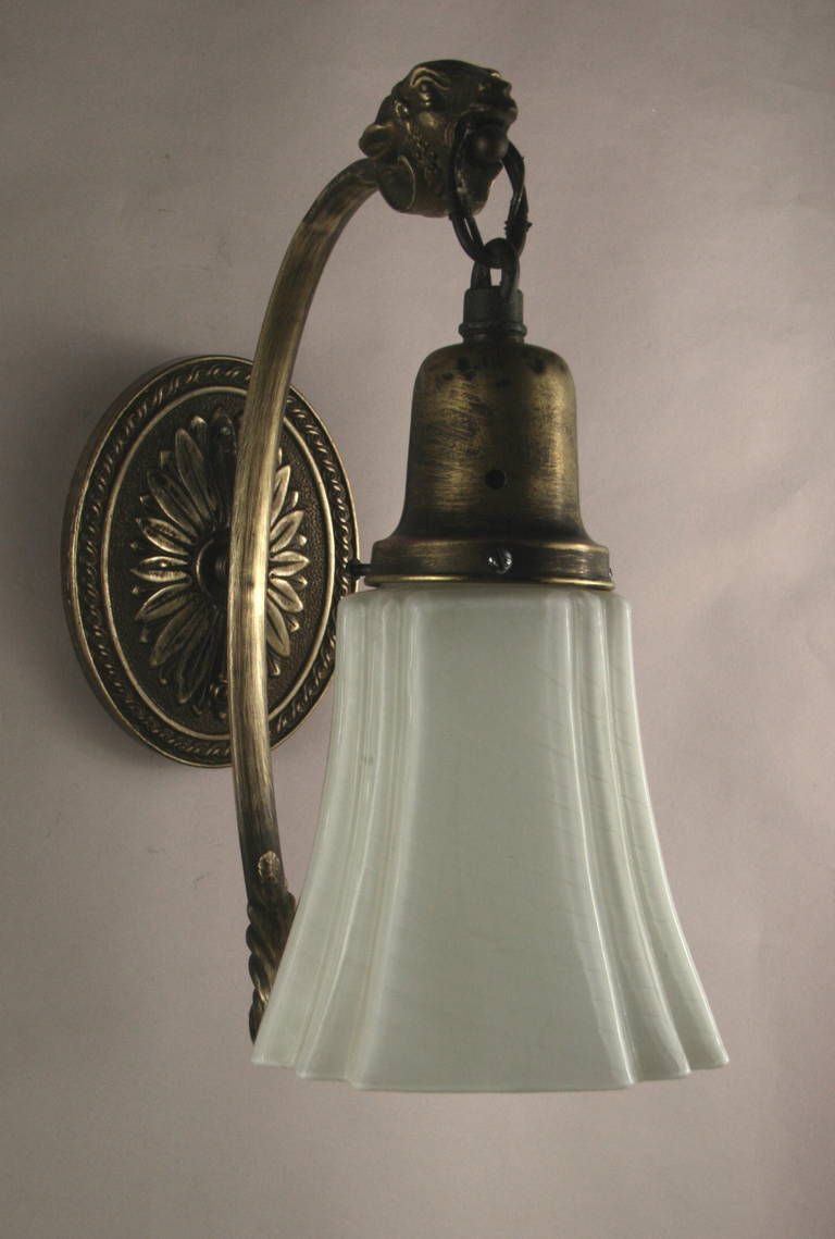 1920s darkened brass single arm sconce ending with a ram head supporting a milk glass shade.