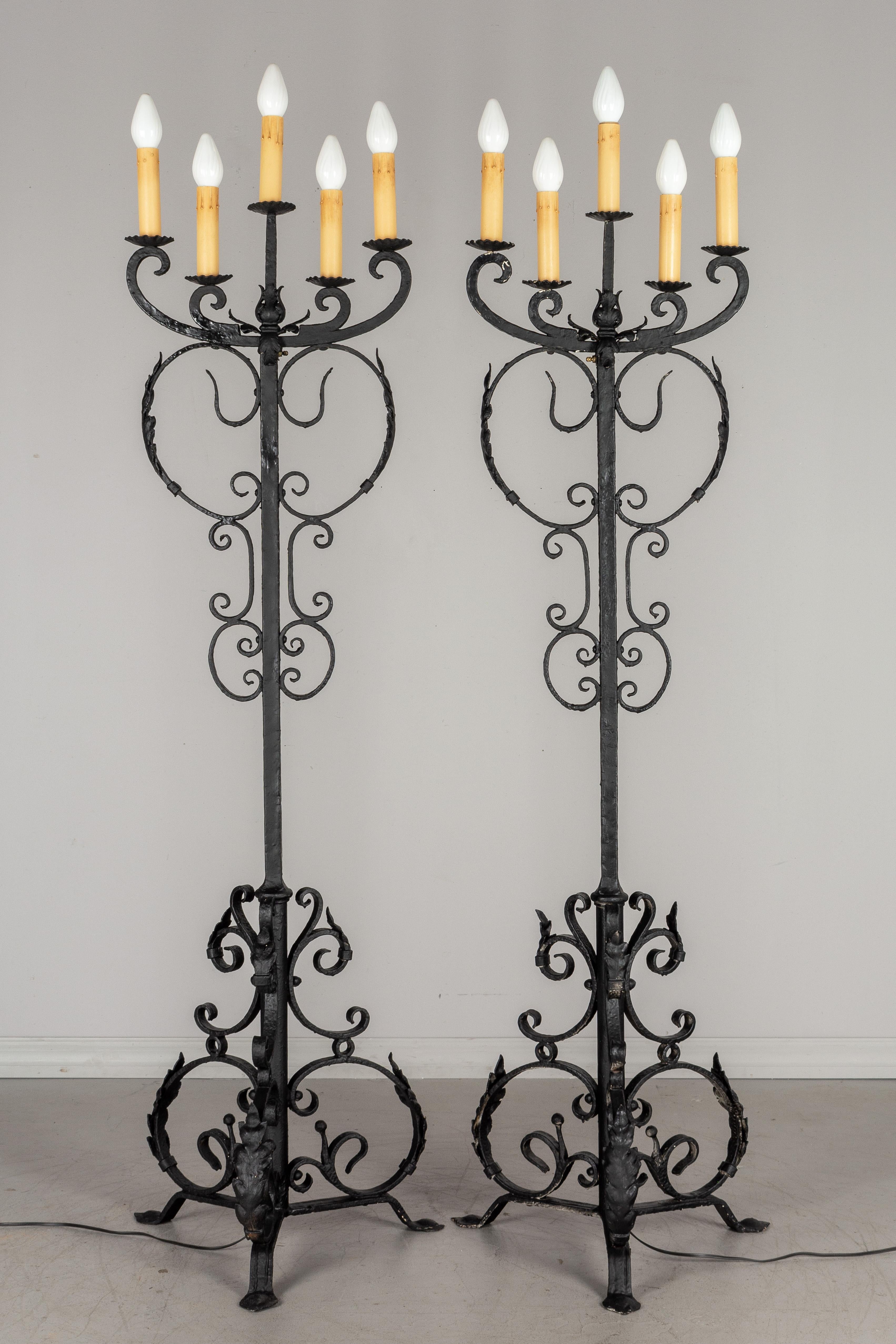 A pair of large Spanish Baroque Revival wrought iron electrified five-light floor torchères with hand forged scrolling iron work and tôle acanthus leaves. Heavy coating of black paint. Rewired and in working condition. Old paper candle covers.