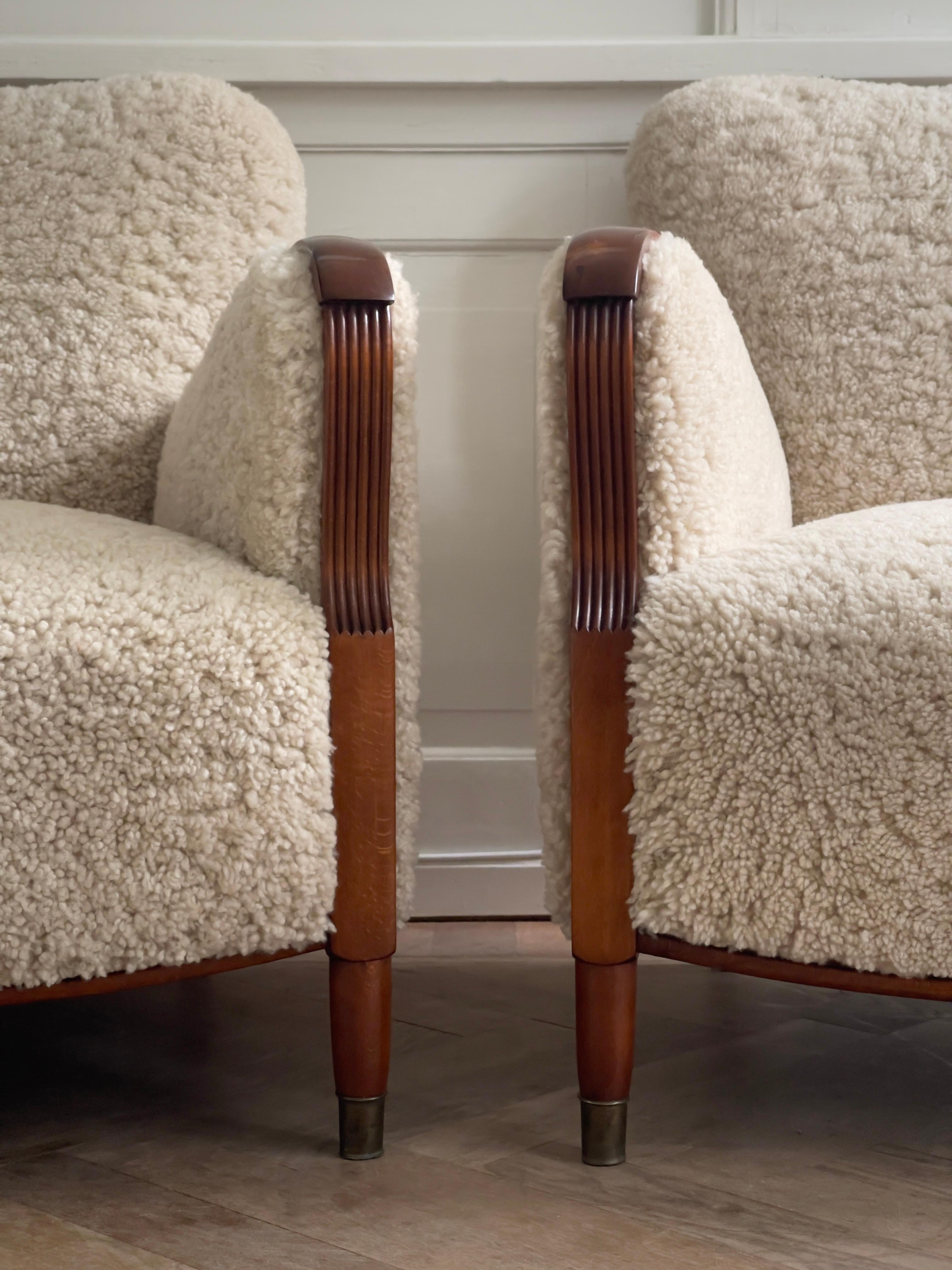 This solid, elegant pair of 1930s Danish lounge chairs represents the sophisticated influence of Art Deco on Danish cabinet-making during the early 20th century. Professionally restored and reupholstered in off-white natural sheepskin, these chairs