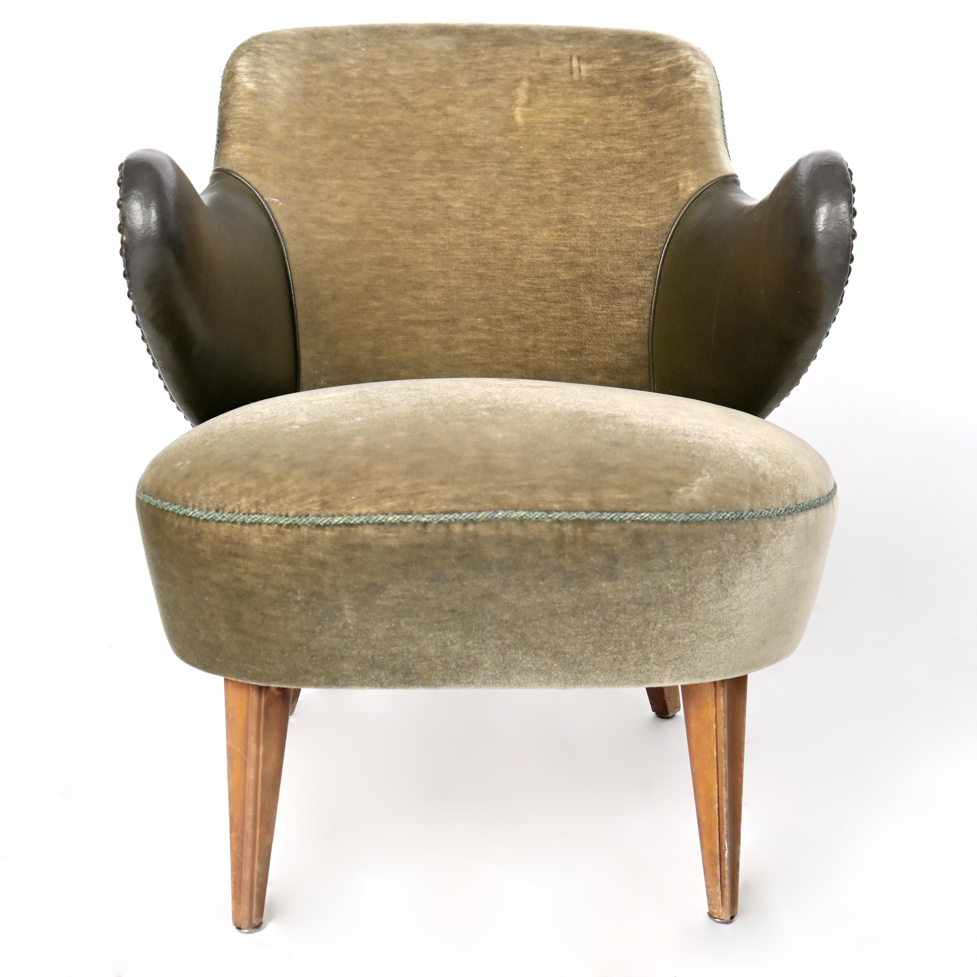 A pair of mix material armchairs. Made with textile fabric with faux leather welted around the upturned curved arms. Rests upon four walnut tapered legs. Circa 1950s. Light stressing and age-related wear in the textile upholstery.
 