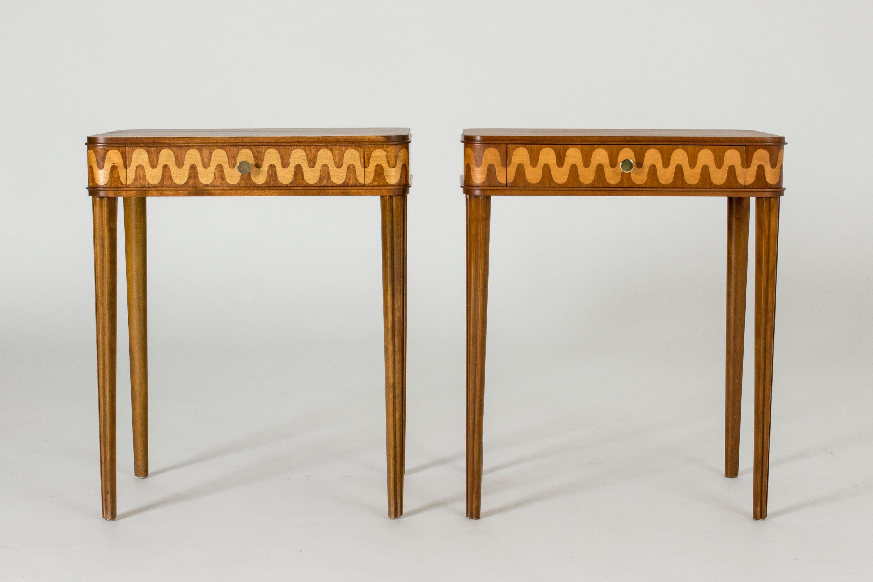 Pair of beautiful bedside tables from NK, with slender tapering legs and drawers with wavy inlays in a lighter wood. This is a married couple, made from different kinds of wood which shows in the different looks of the woodgrain.