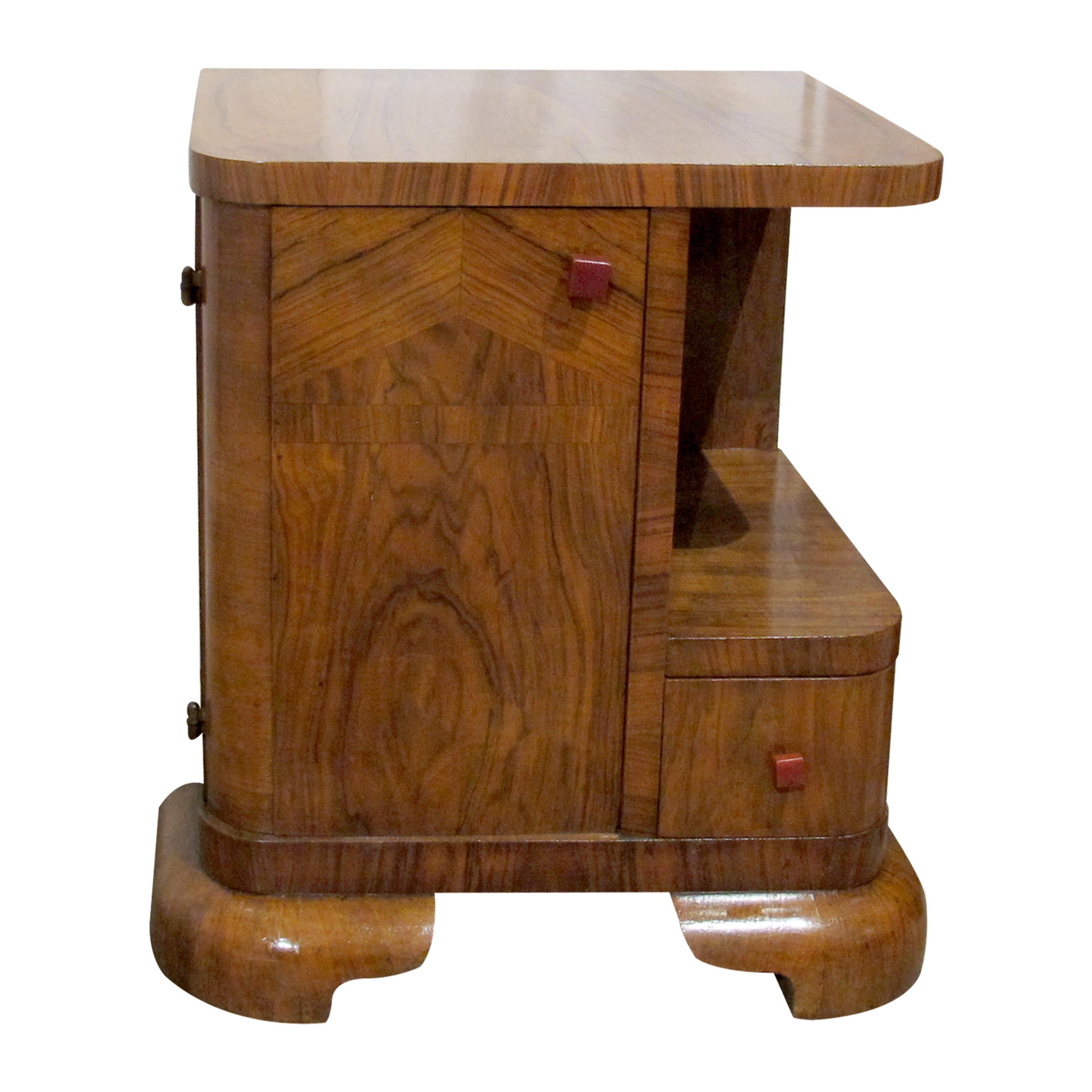 A charming pair of 1930s walnut Belgian Art Deco bedside tables. Each table features smooth, rounded edges, decorative veneer patterns, and sturdy curved feet. The design includes an open shelf, a small drawer with square Bakelite handles, and a