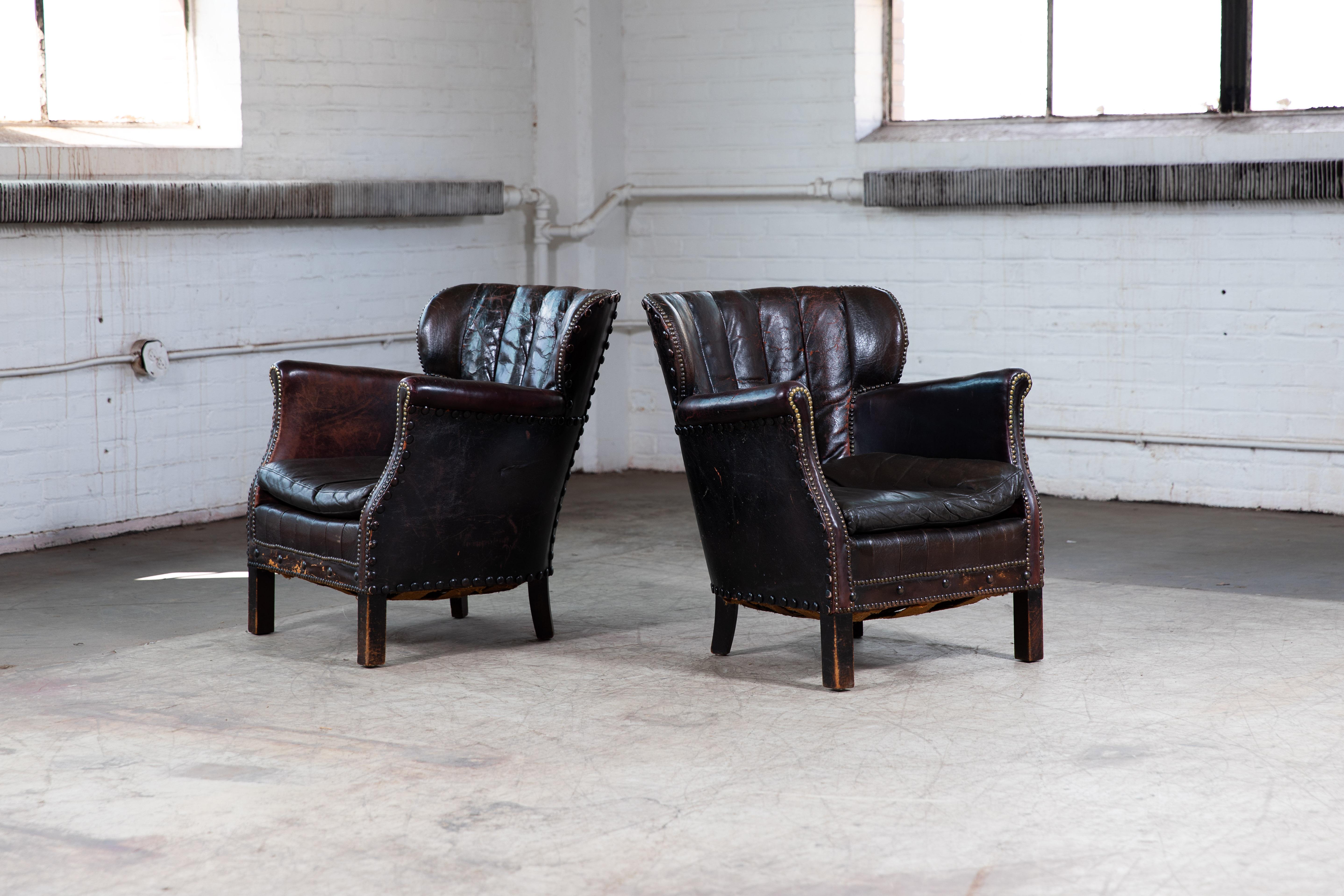 Charming pair of small scale Danish club armchairs attributed to Danish Furniture Maker Oskar Hansen around the mid-1930s. Covered in original black leather with tufted back with some red and brown colors peaking through herre and there where the
