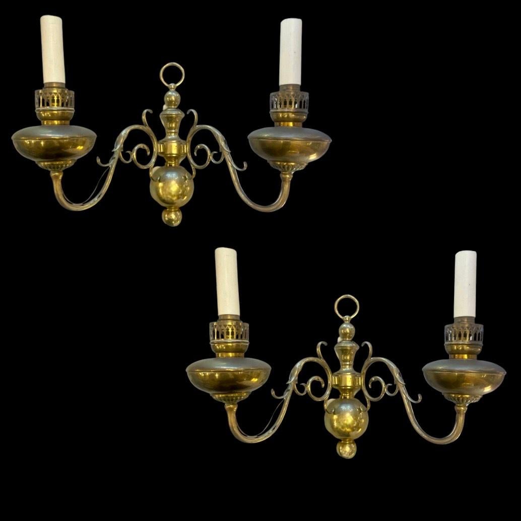 Exquisite aged brass Dutch Flemish 1930 wall sconces.

Embodying the essence of traditional Dutch Flemish style, each sconce boasts two enchanting scrolling arms, crowned with a distinctive ring, and anchored by bulbous bases adorned with a charming