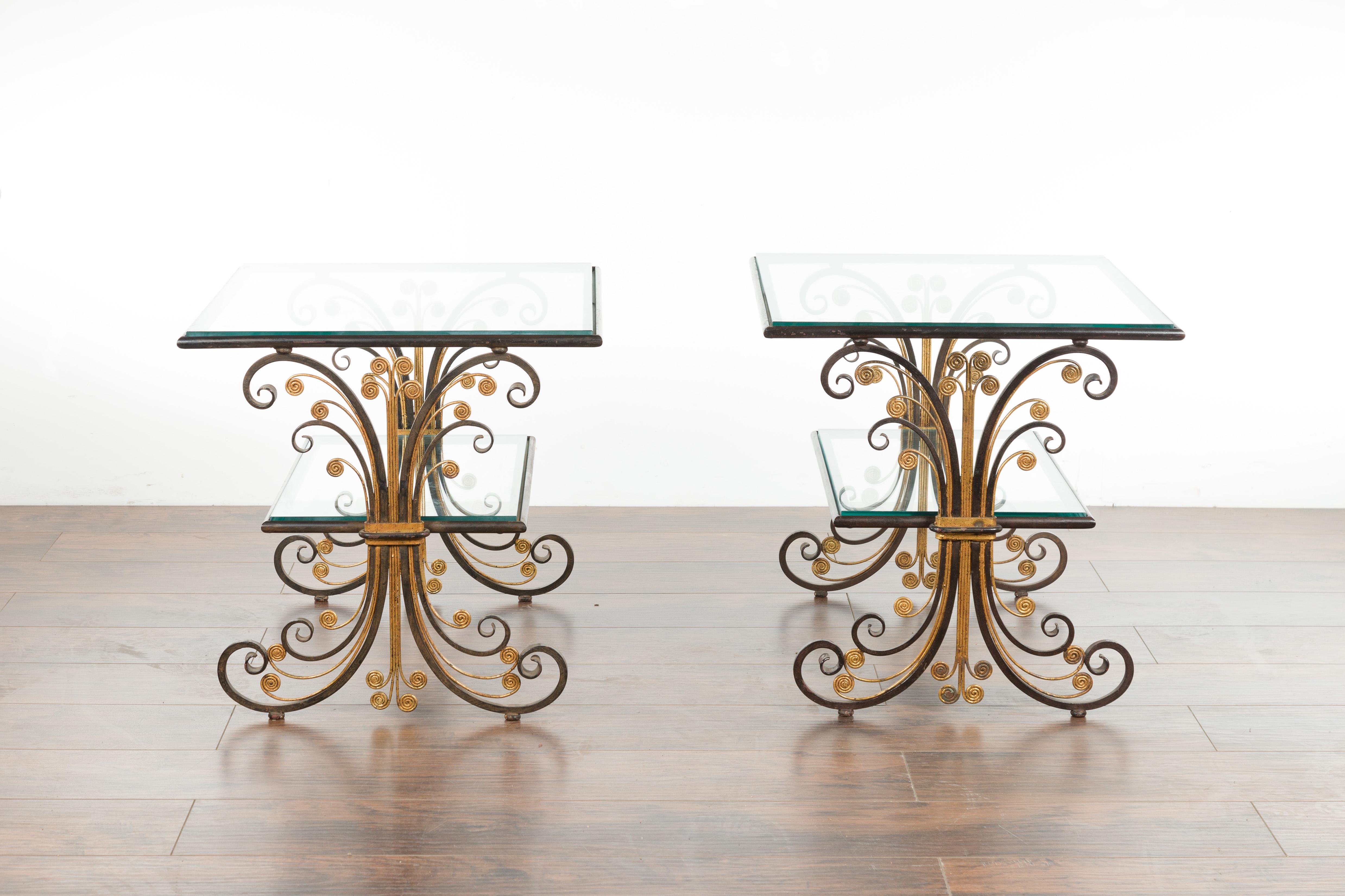 A pair of French Art Deco period iron and brass side tables from the mid-20th century, with scrolling effects and glass tops. Created in France during the second quarter of the 20th century, each of this pair of side tables features a rectangular