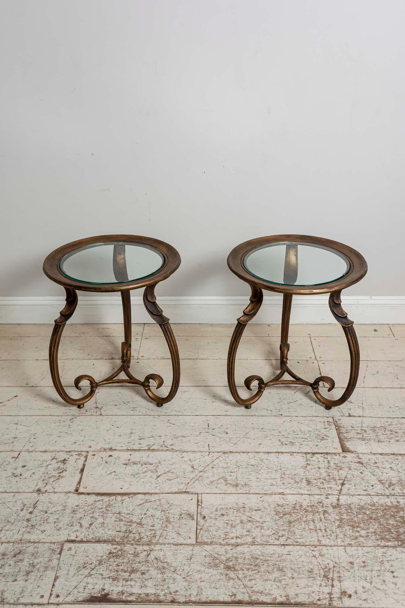 Pair of stylish bronzed metal side tables with glass insert table tops. The three legs scroll inwards and connect to a triangular shaped piece of bronzed metal. A two-stepped decoration features at the top of each leg.

The tables are most likely