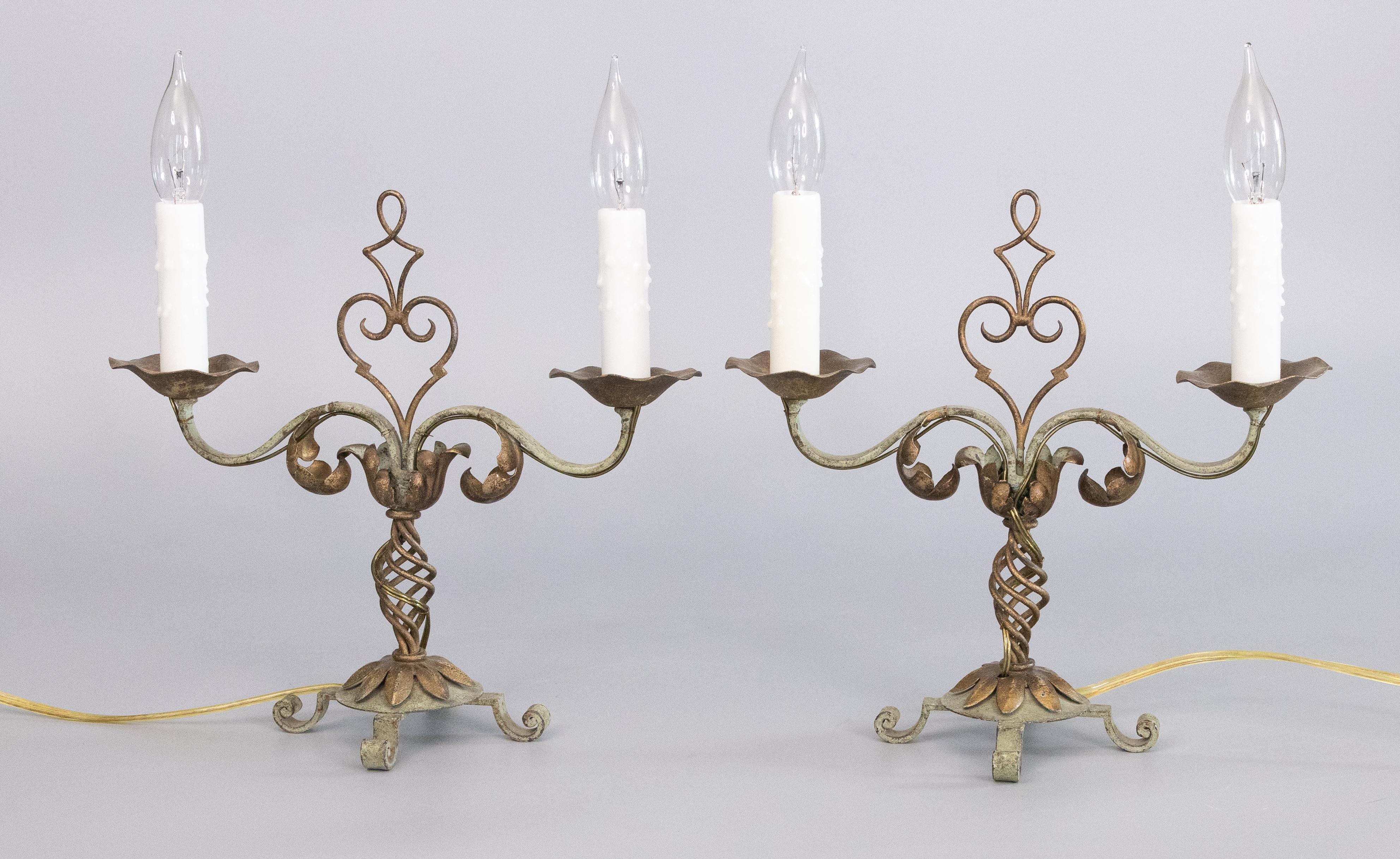 A gorgeous pair of 1930s French gilt tole and iron two light candelabras table lamps. These beautiful lamps are hand painted with lovely gold and light verdigris colors and accented with drippy wax candle sleeves. They are in excellent working