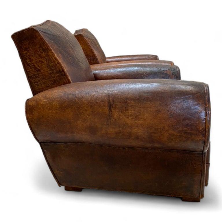 Ces fauteuils club en cuir français des années 1930 sont recouverts de cuir de haute qualité en bon état vintage avec un caractère bien usé. 
Avec leurs accoudoirs emblématiques en forme de cigare et leur dossier unique en forme de moustache, ces