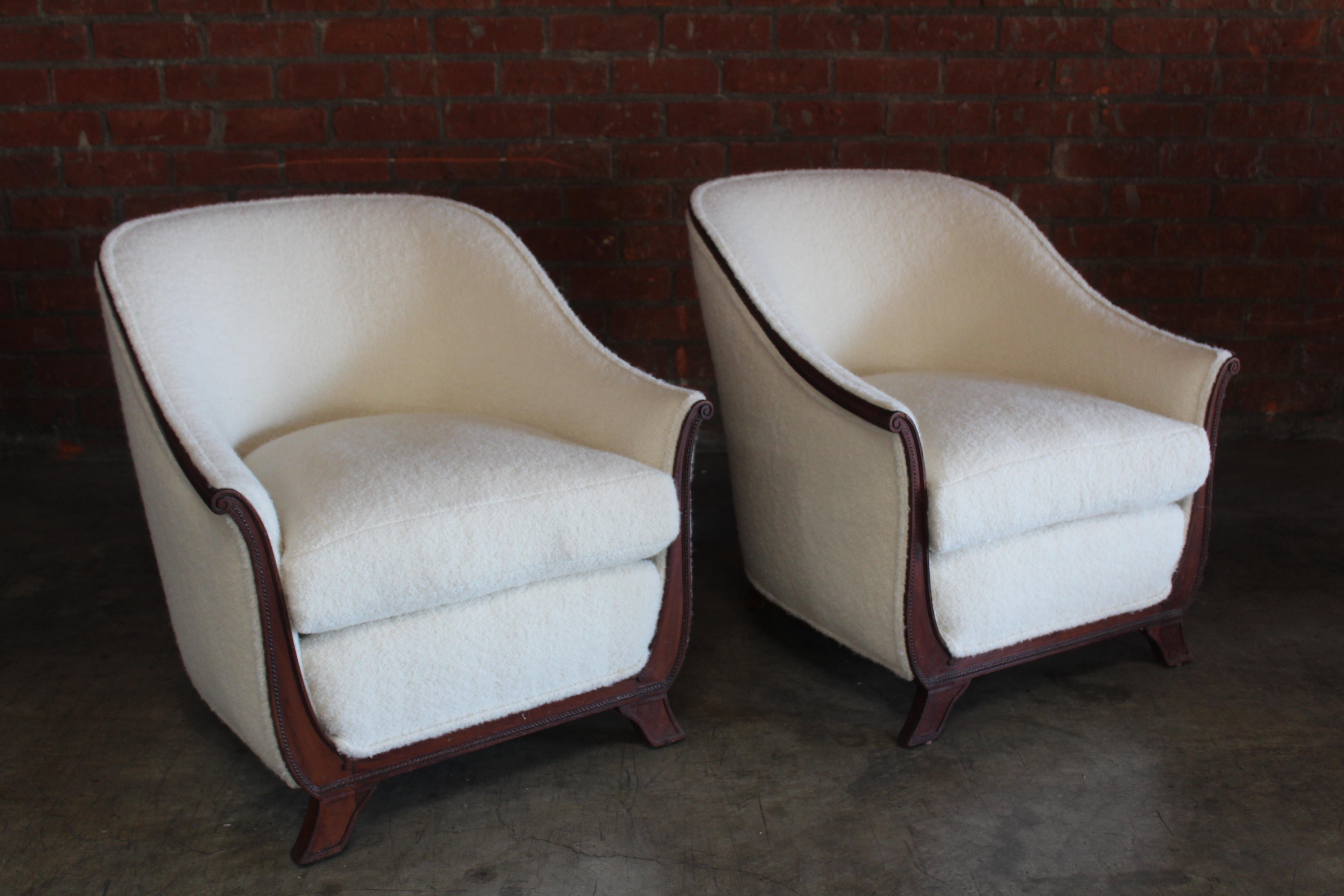 Pair of 1930s lounge chairs from France. They feature mahogany frames with intricate carved details. They have been reupholstered in a new alpaca wool boucle. They are in wonderful condition. The mahogany trim shows minor signs of wear.