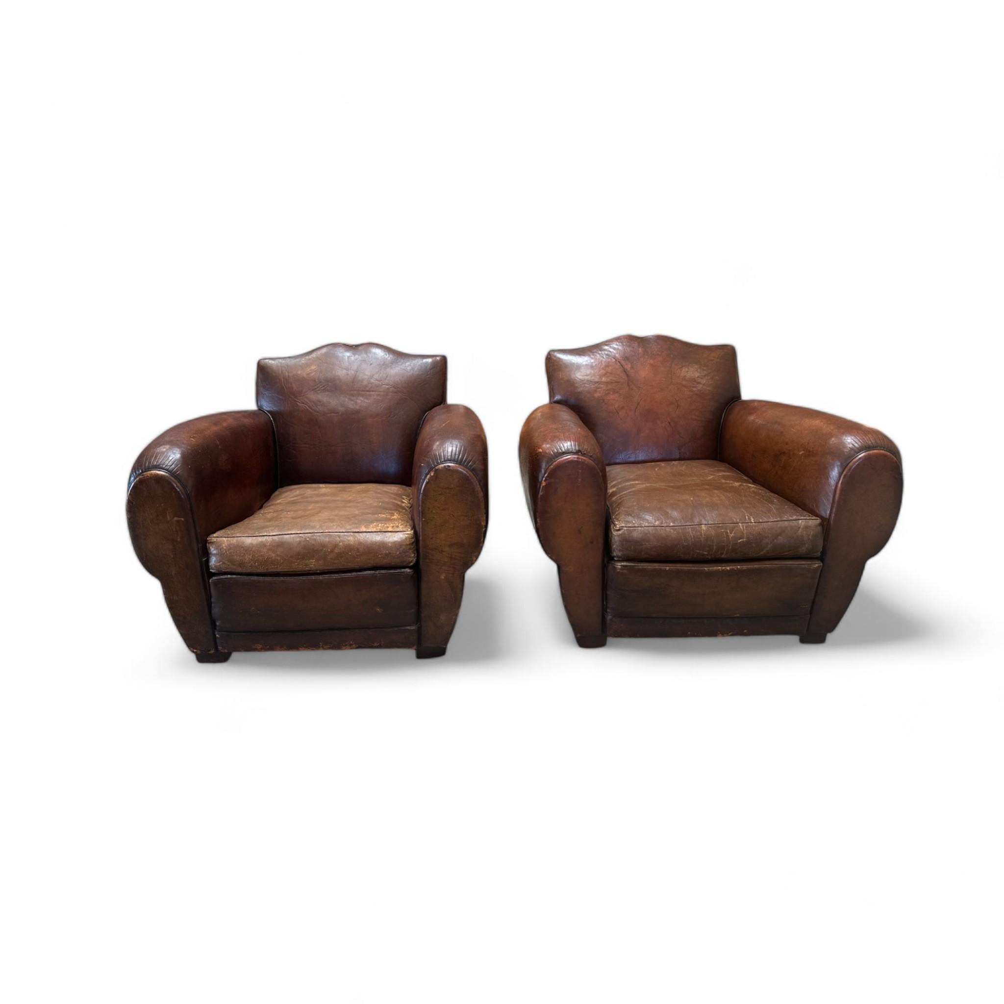 This pair of 1930s French Mustache Club Chairs features a classic Art Deco design, with beautifully aged patina on rich, brown leather. The chairs boast the signature 