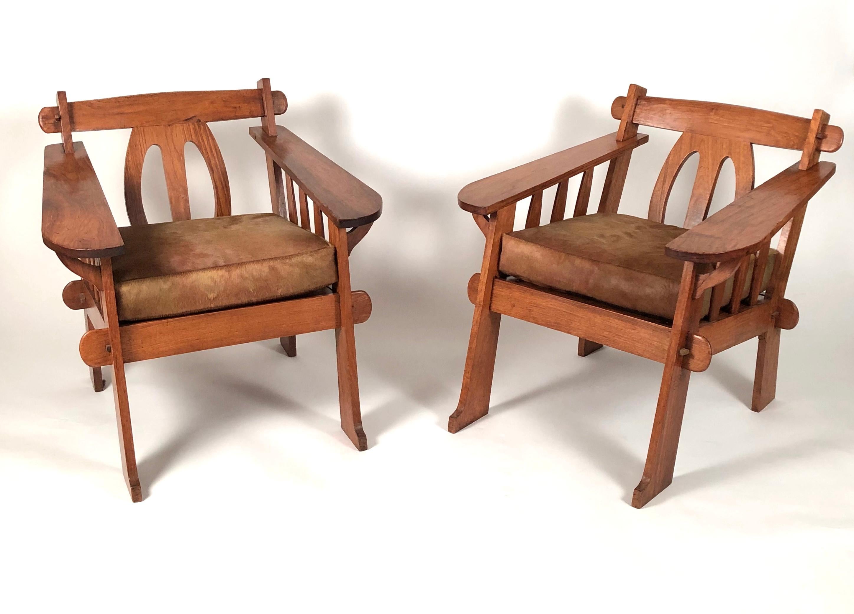 A beautifully made pair of Hawaiian teak lounge chairs, made for shipboard travel, circa 1930s, with mortise and tenon construction, each back with geometric oval splats, flanked by wide paddle arms above a slatted seat with loose deer hide seat