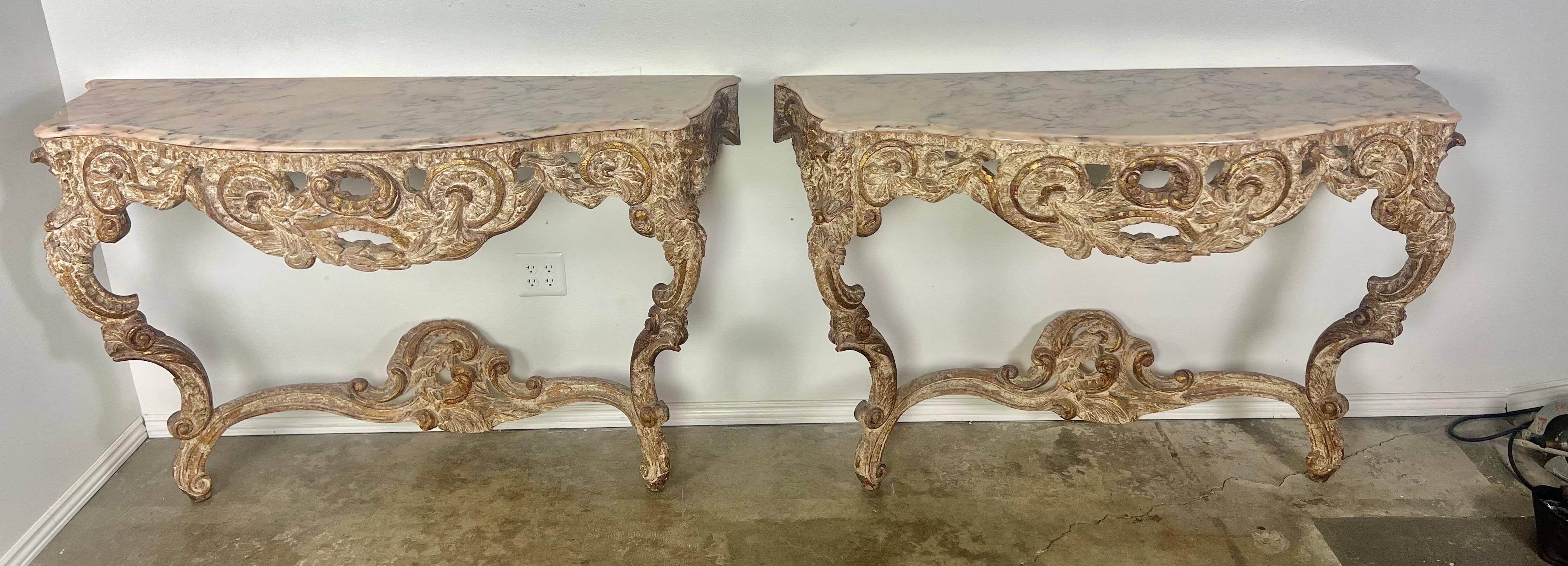 Pair of 1930's giltwood Italian Rococo style consoles with marble tops.  The ornately carved wood consoles stand on cabriole legs.  Laurel leaves, acanthus leaves and scrolls can be seen in the intricate carving.  The consoles are topped with the