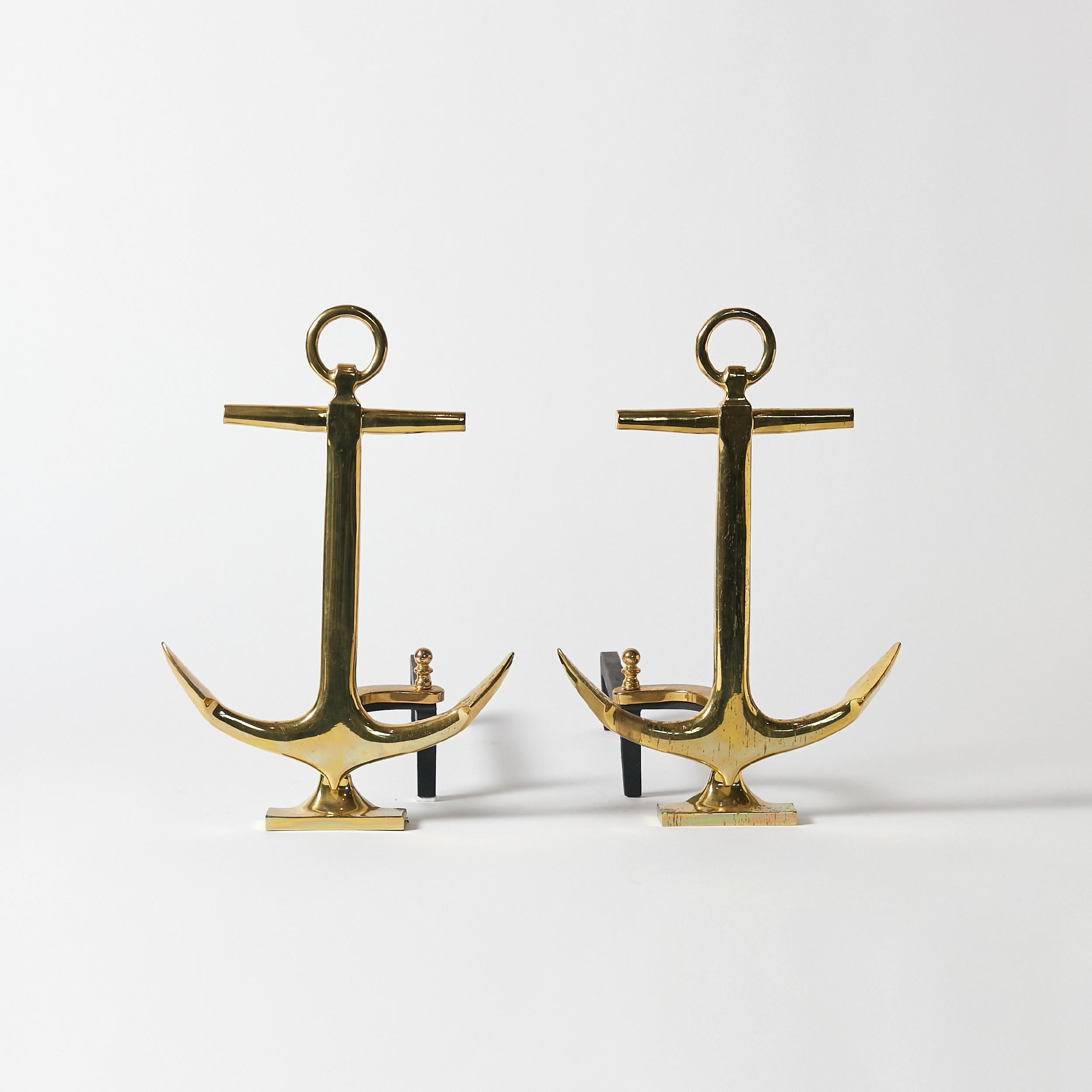 Pair of anchor-shaped andirons in polished brass with black iron stand. Made in USA, circa 1940.