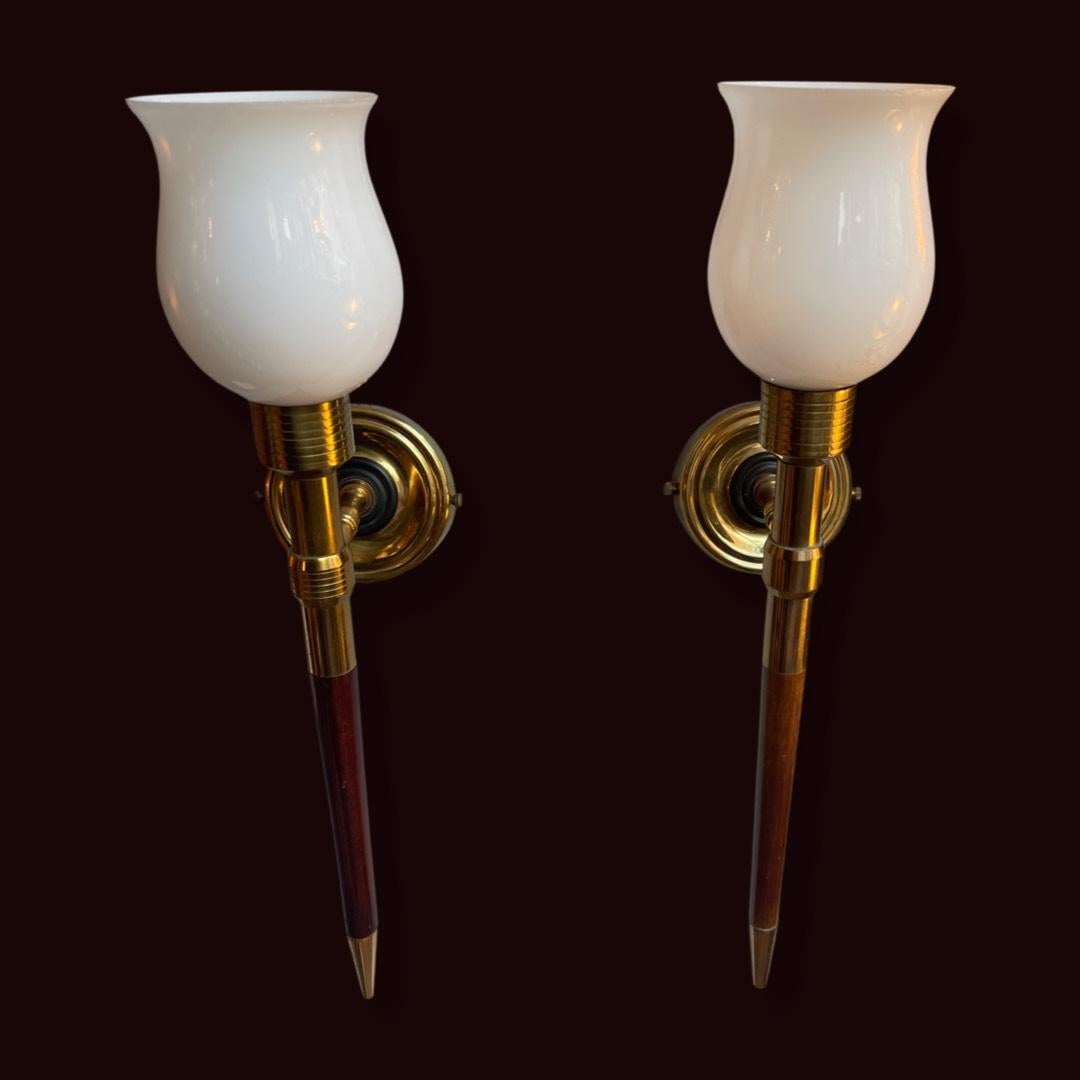 Apliques franceses de latón y madera de las décadas de 1940 a 1950, que irradian elegancia y sofisticación atemporales. Fabricados en forma de antorcha, estos cautivadores apliques cuentan con opulentas pantallas de cristal opalino que añaden un