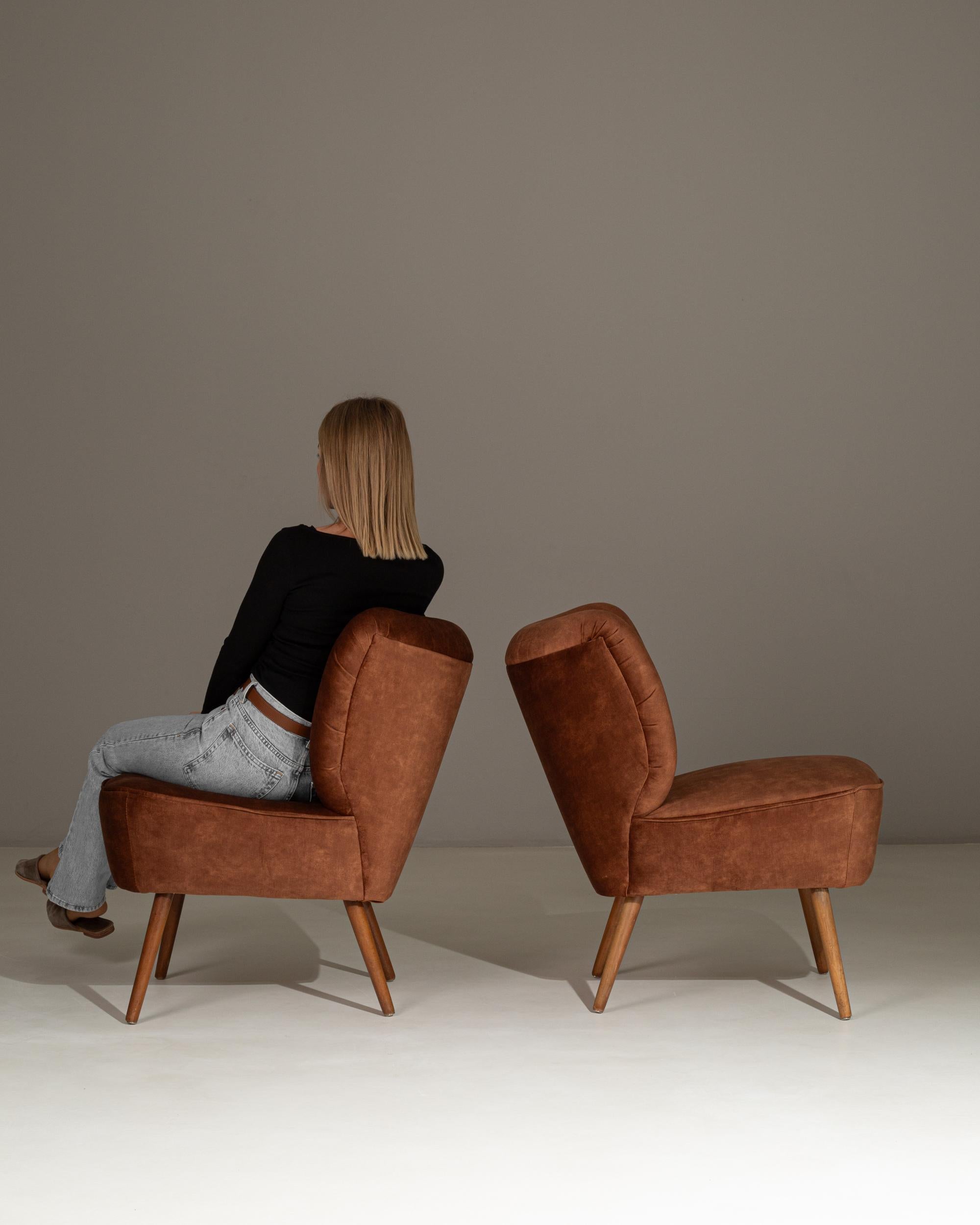 This pair of 1940s Danish cocktail chairs showcases the elegant, sculptural lines characteristic of mid-century Scandinavian design. The gently flared backs feature vertical channel tufting that adds both texture and refinement, while the warm brown
